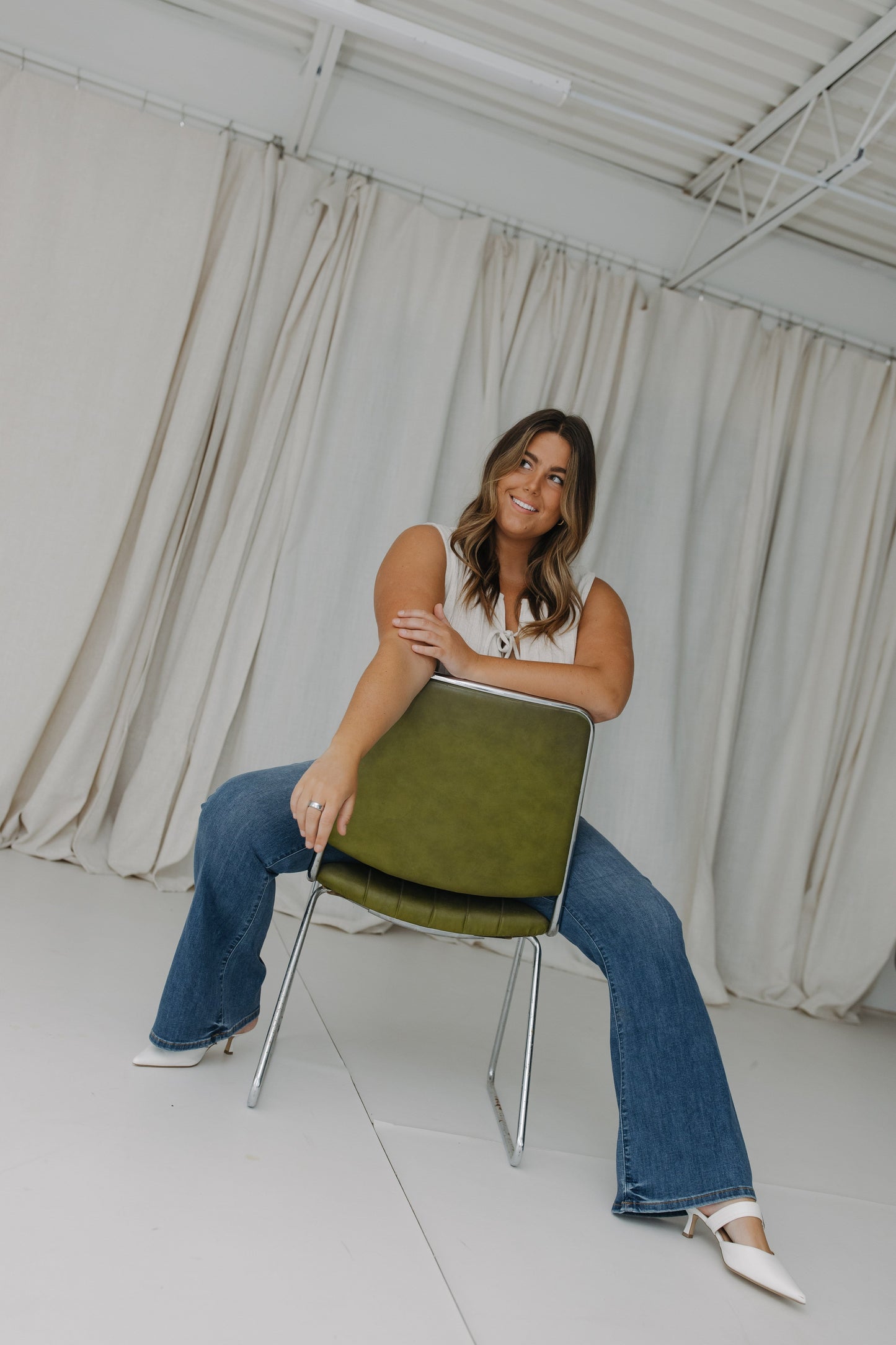 Woman sitting on a green chair in a room with white curtains