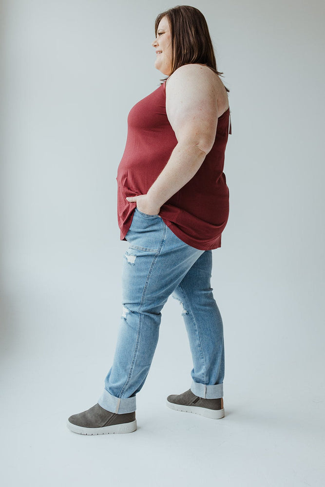 Person wearing a maroon sleeveless top and Judy Blue High Waisted Destroyed Boyfriend Jeans in Medium Wash stands sideways against a plain white background, effortlessly pulling off the cool girl look.