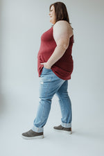 A person stands with their back turned, showcasing a cool girl look in a red sleeveless top, Judy Blue High Waisted Destroyed Boyfriend Jeans in Medium Wash, and grey slip-on shoes.