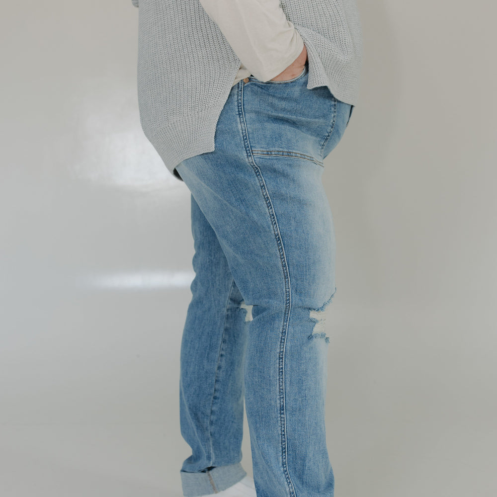 Person wearing light blue jeans and a gray sweater on a plain background