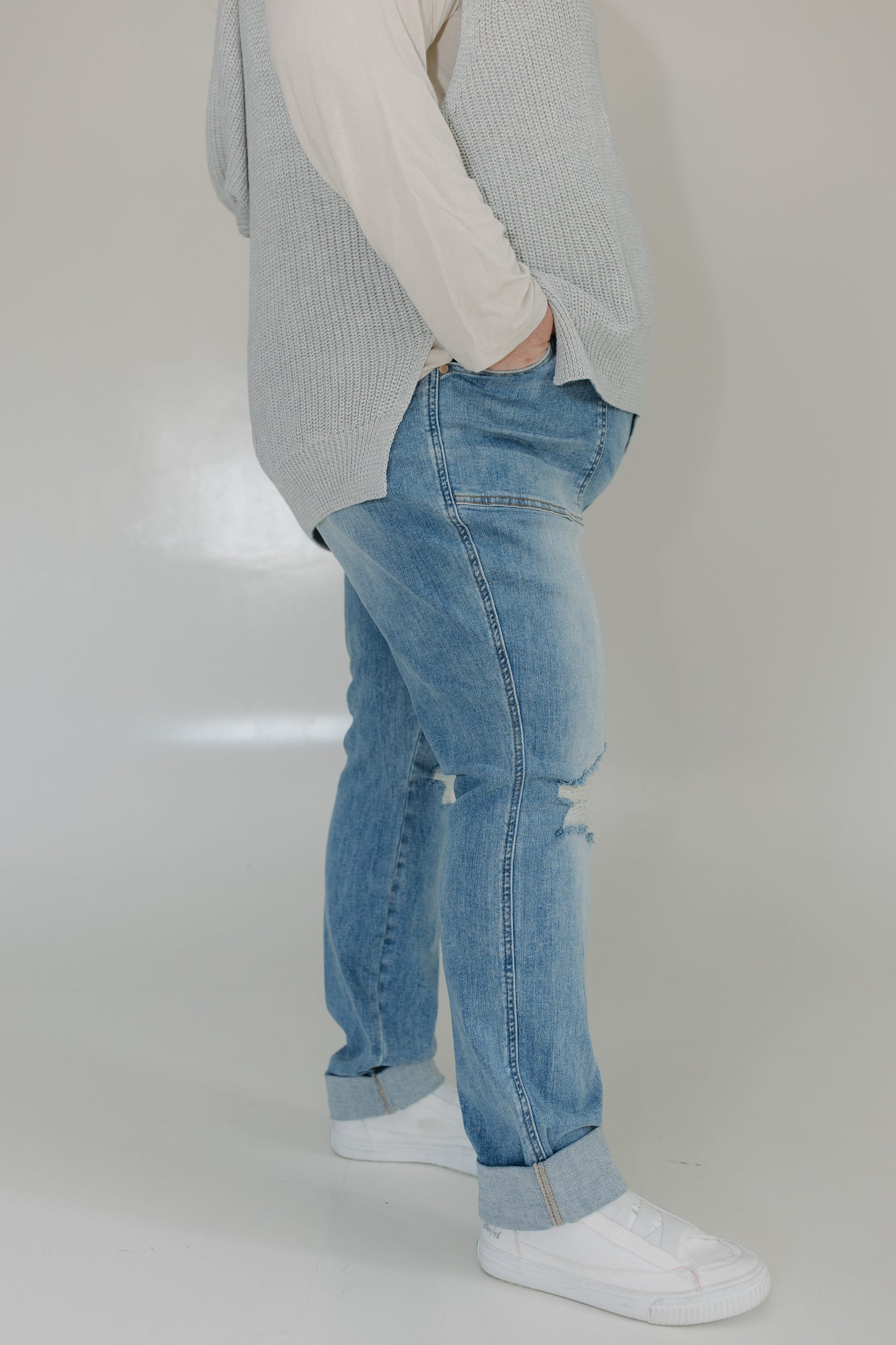Person wearing light blue jeans and a gray sweater on a plain background