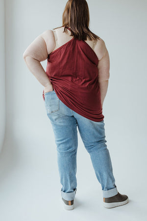 A person stands with their back turned, showcasing a cool girl look in a red sleeveless top, Judy Blue High Waisted Destroyed Boyfriend Jeans in Medium Wash, and grey slip-on shoes.