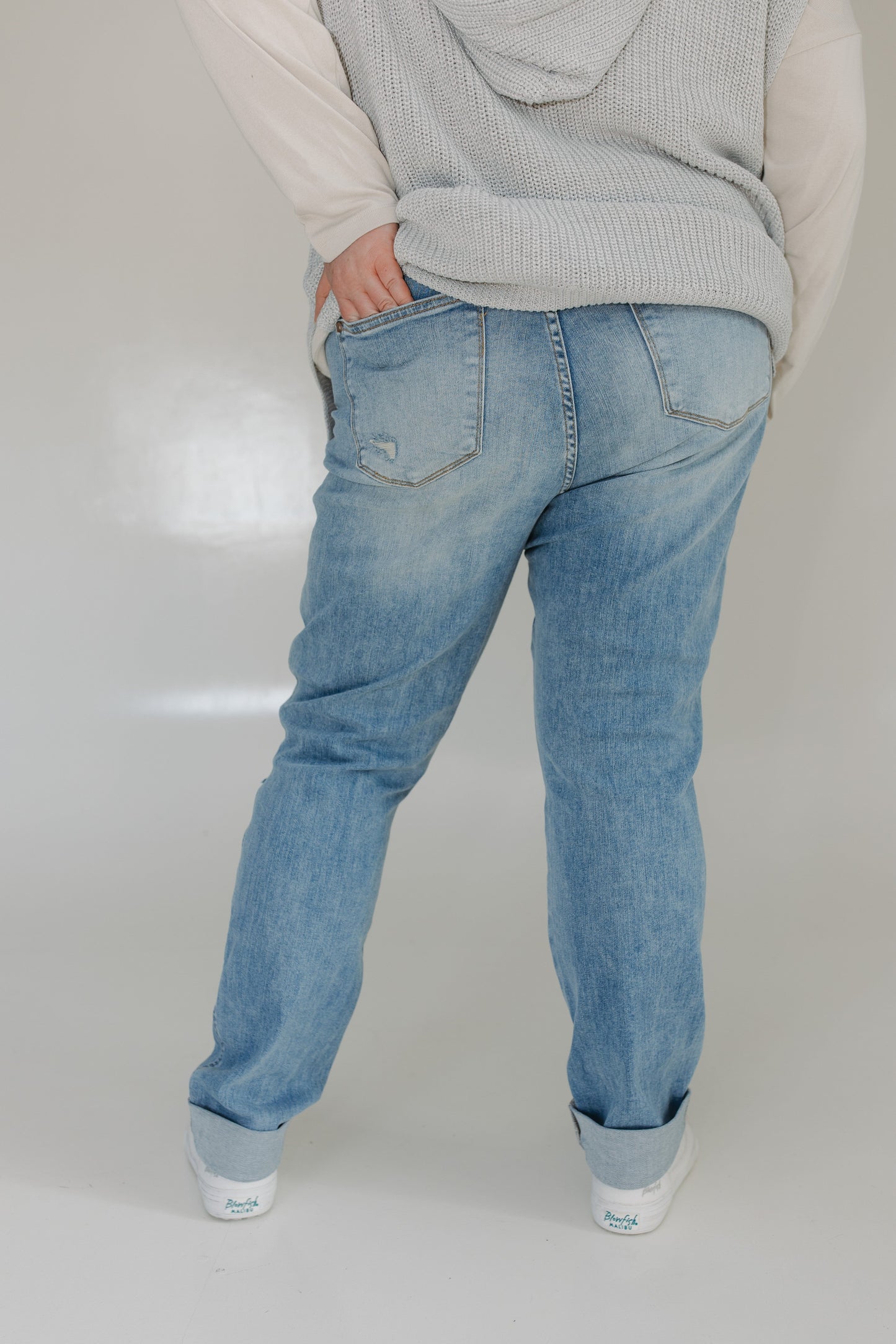 Person wearing light blue jeans and a gray sweater on a plain background