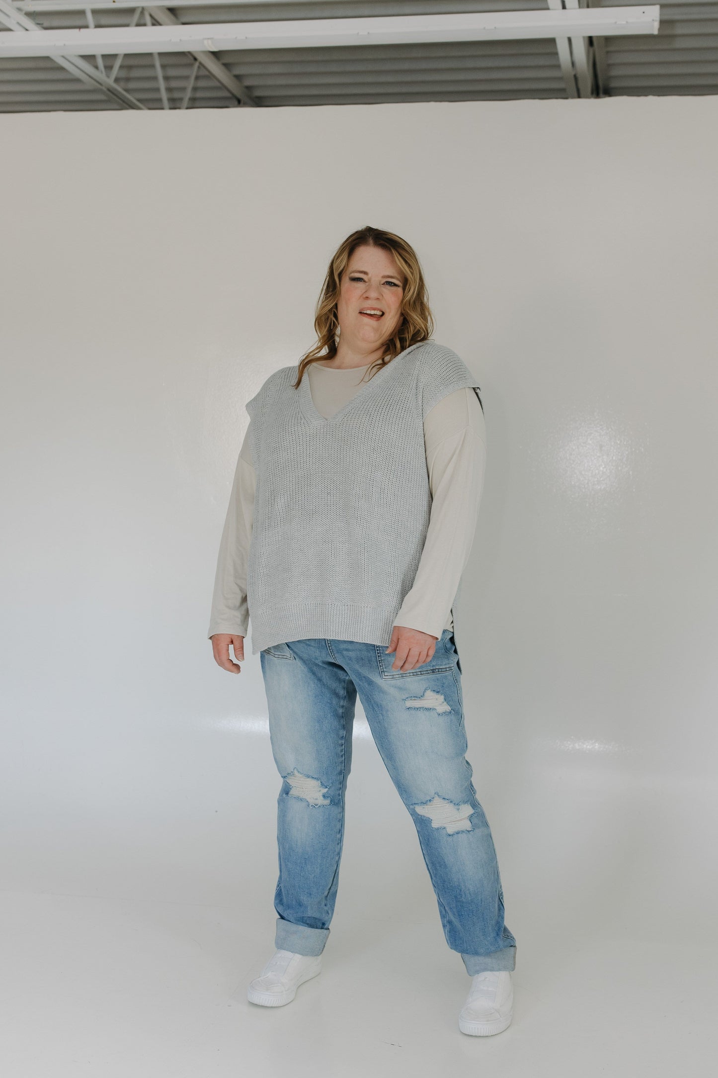 Person wearing a light gray sweater and blue jeans standing against a white background