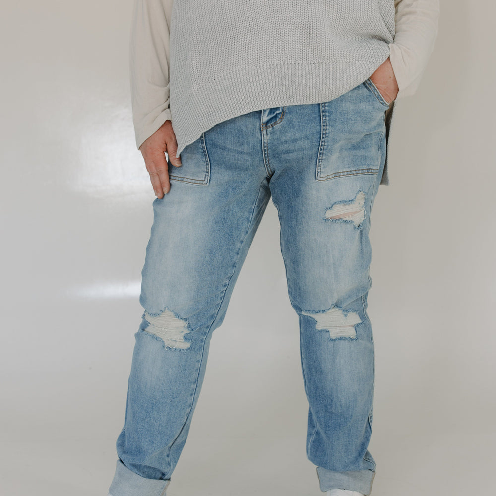 Person wearing light blue ripped jeans and a gray sweater on a plain background