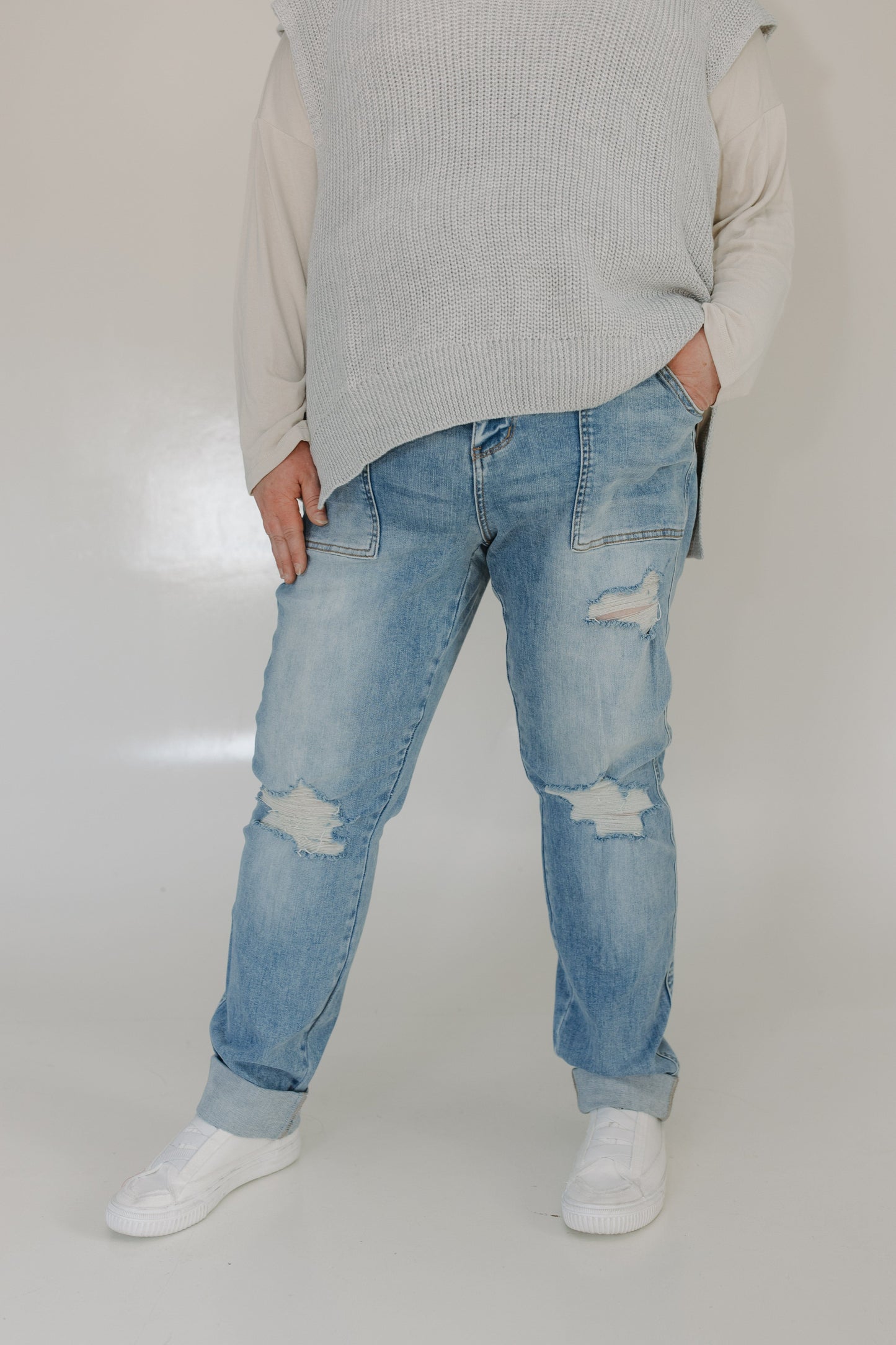 Person wearing light blue ripped jeans and a gray sweater on a plain background