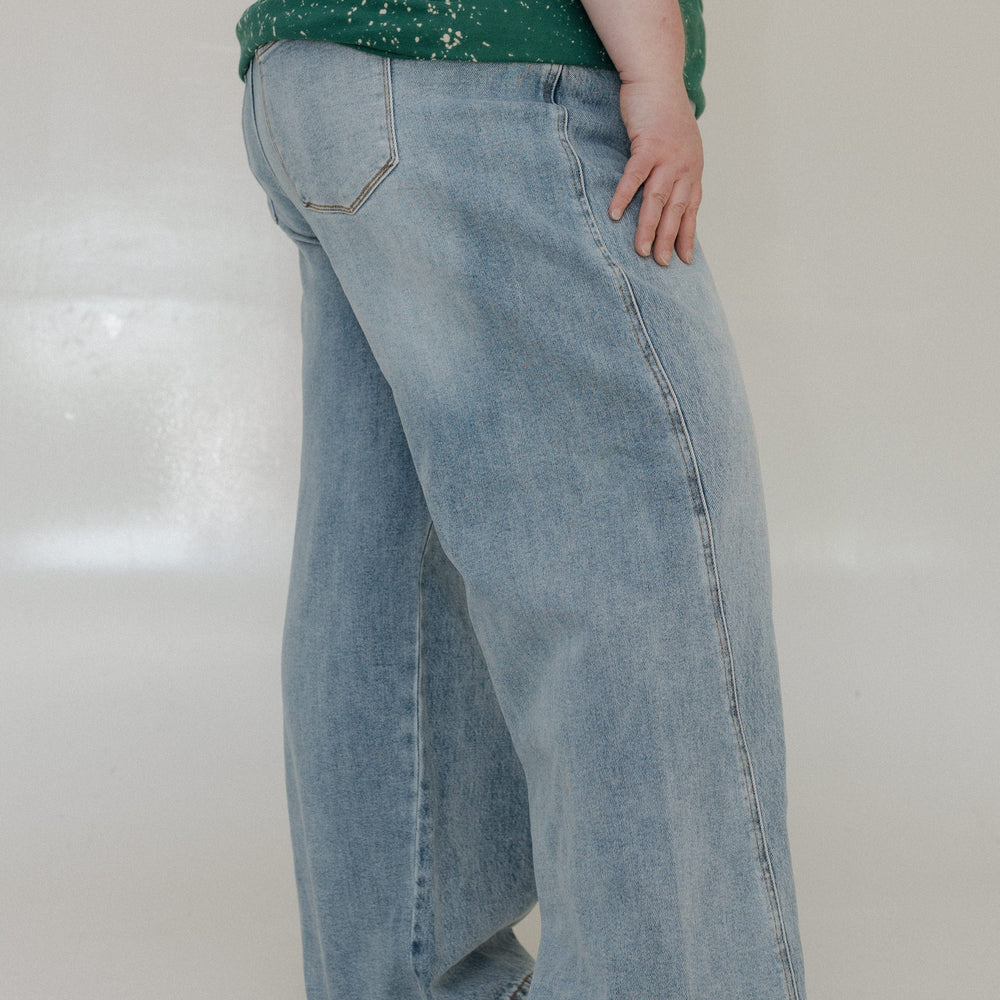 Person wearing light blue jeans and a green top on a white background