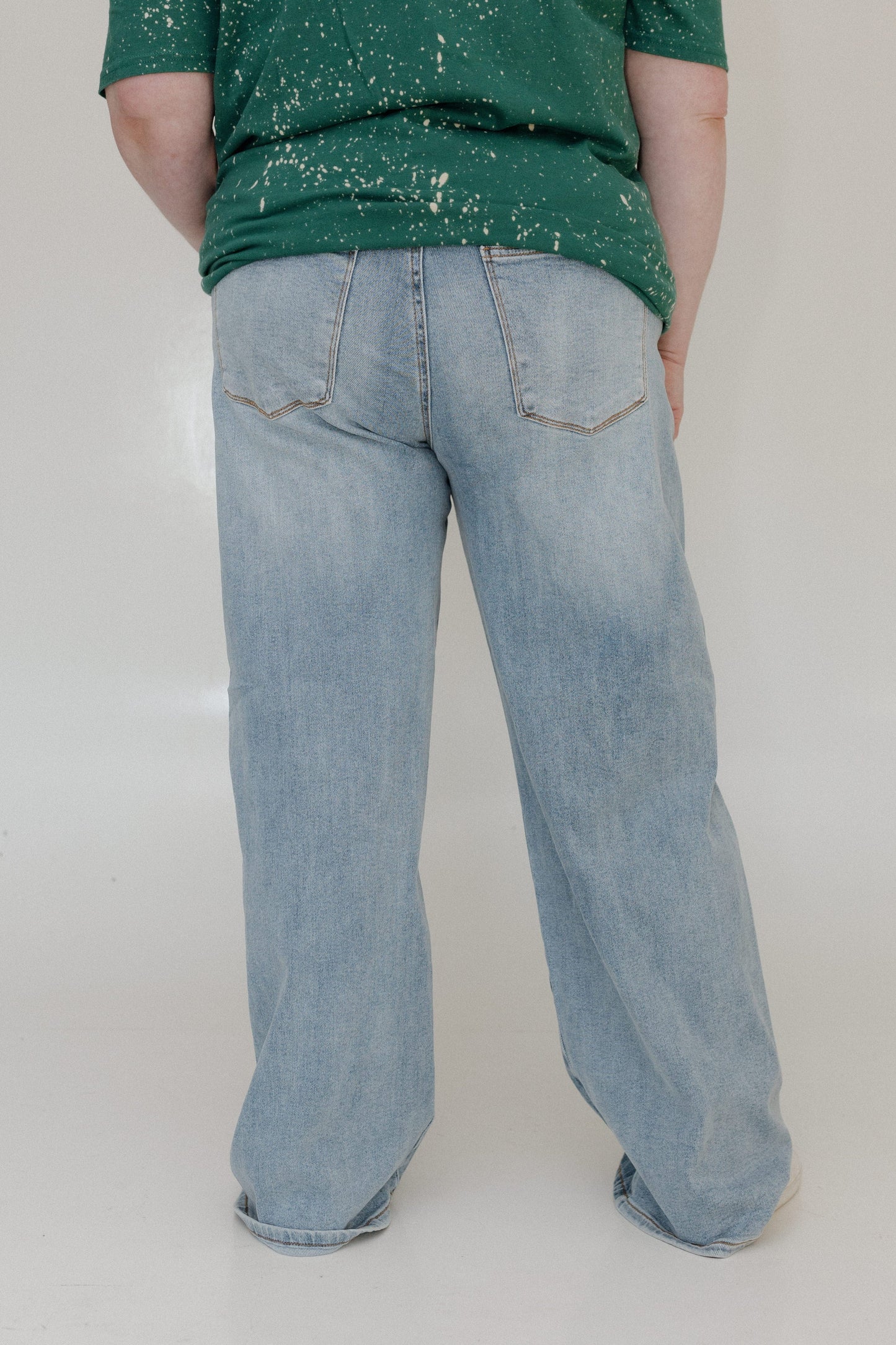 Person wearing a green splatter-painted shirt and light blue jeans on a plain background