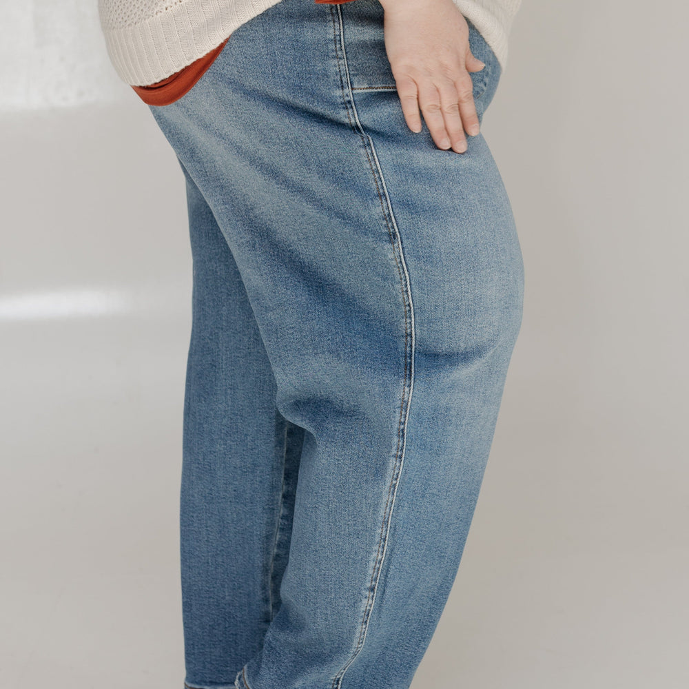 Person wearing blue jeans and a beige sweater with a red shirt underneath on a white background