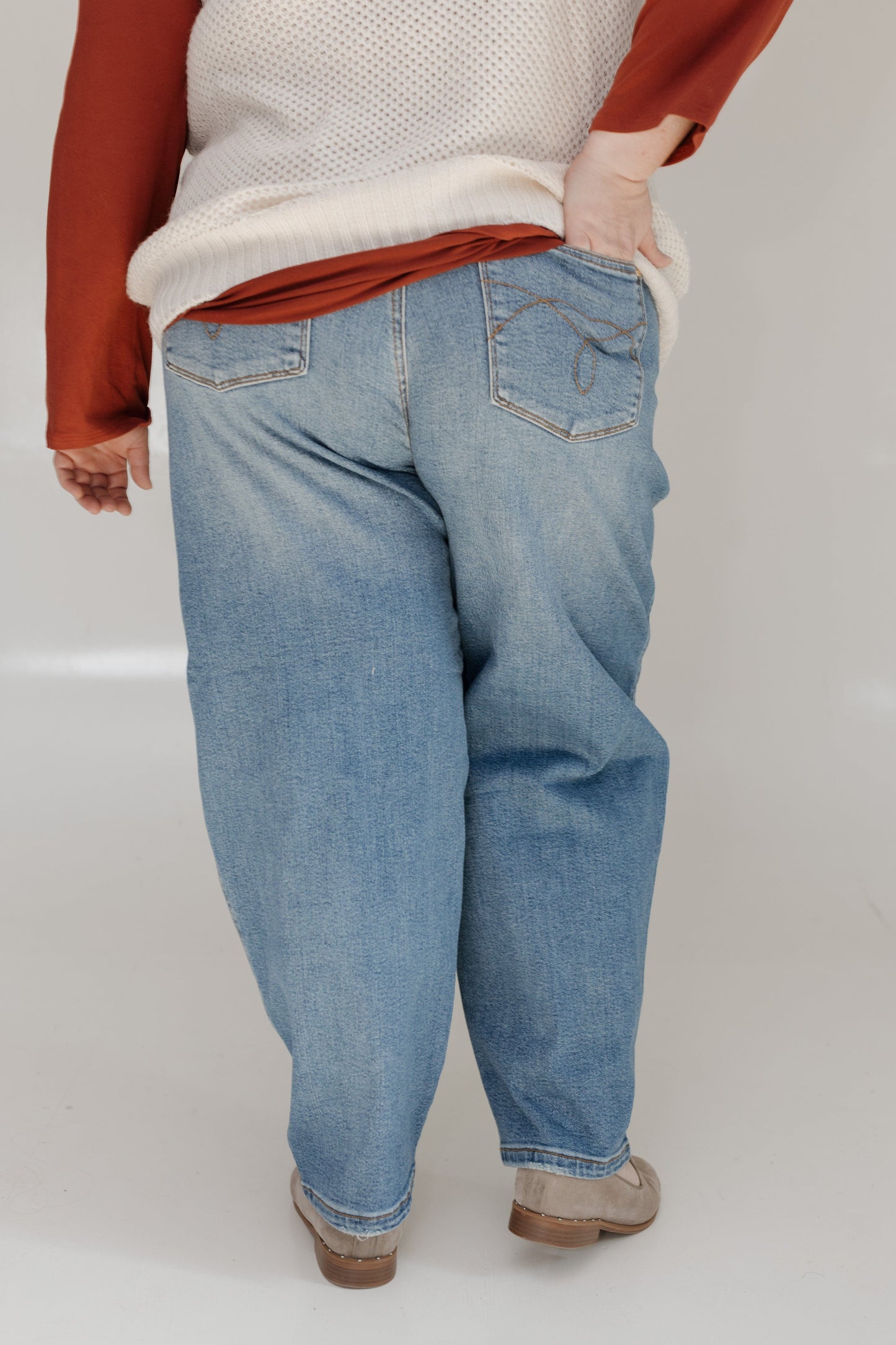 Person wearing blue jeans and a white sweater with red sleeves on a plain background