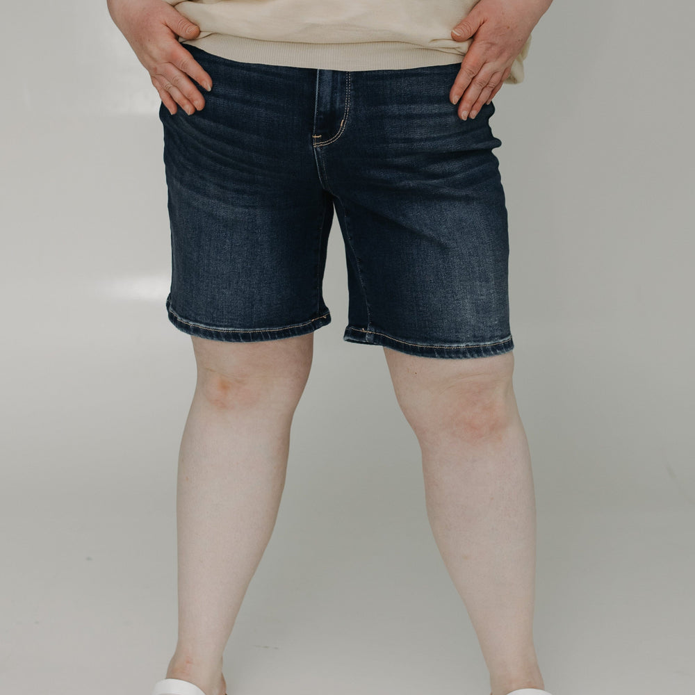 Person wearing blue denim shorts and a beige top on a plain background