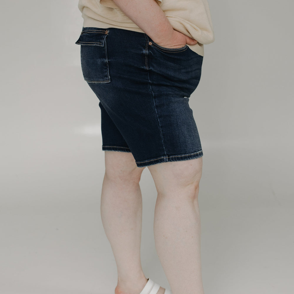 Person wearing a beige sweater and dark denim skirt on a plain background