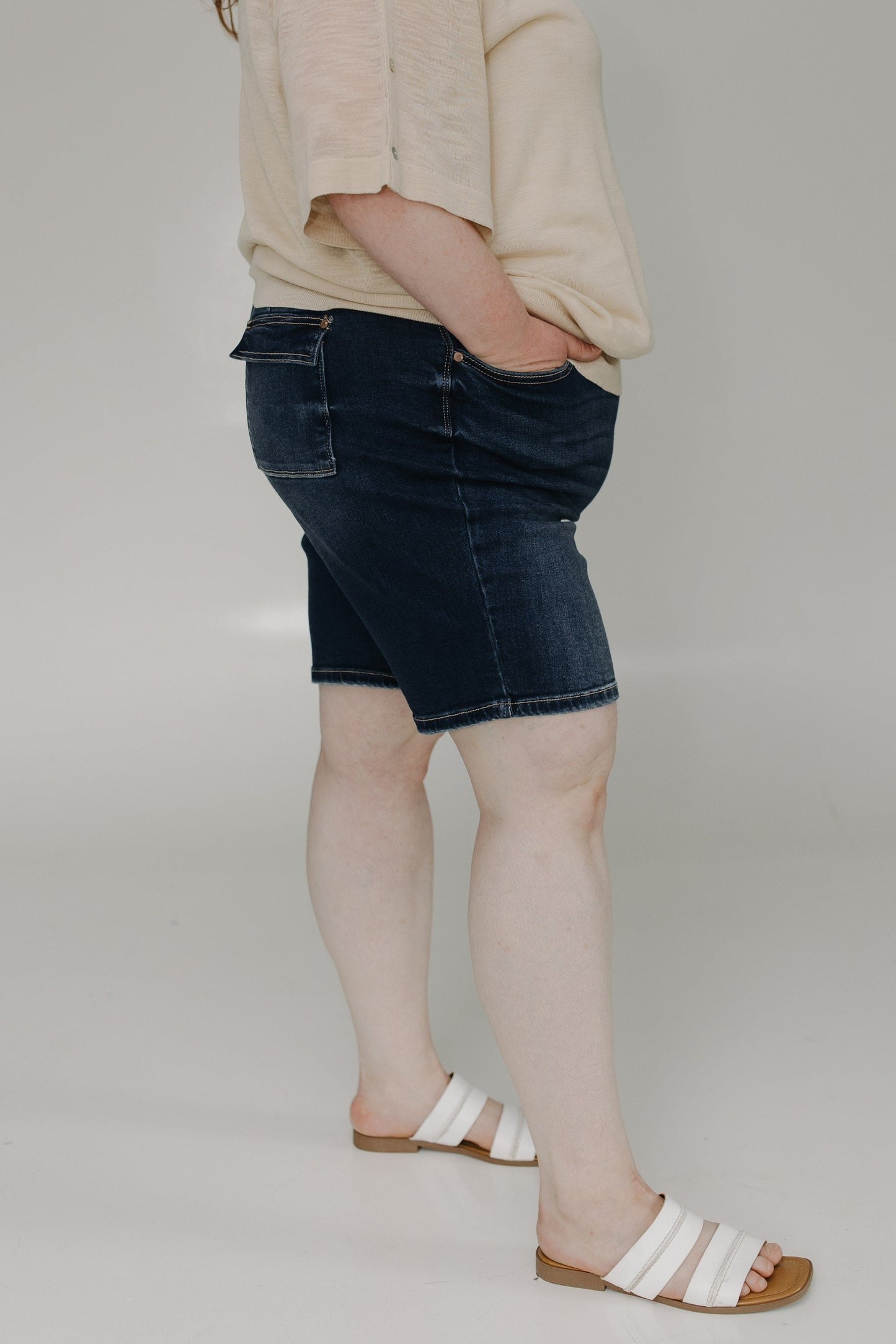 Person wearing a beige sweater and dark denim skirt on a plain background