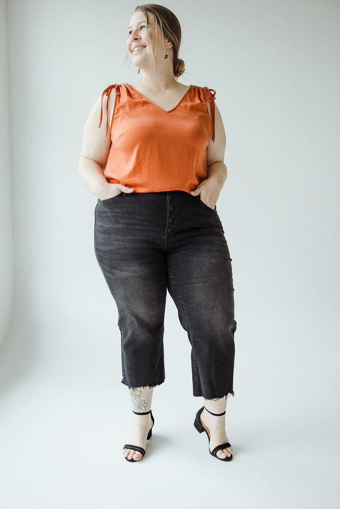 A person stands facing away, wearing a sleeveless orange top and high-waisted Judy Blue JUDY BLUE HIGH WAIST BUTTON FLY RAW HEM CROPPED WIDE LEG jeans. They have short hair and are positioned against a plain background.