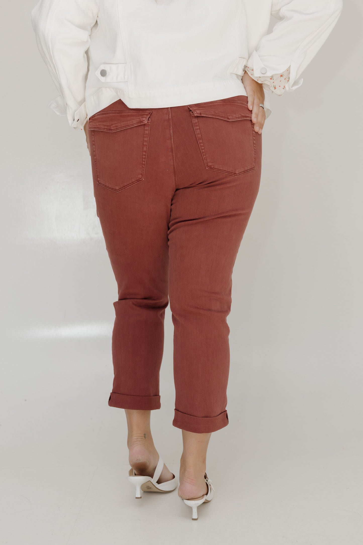 Person wearing rust-colored pants and a white top on a plain background