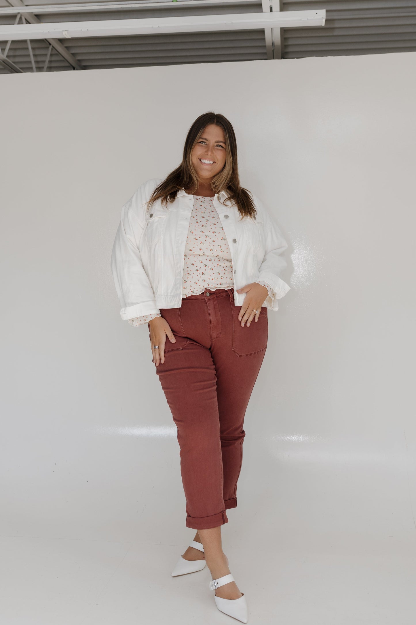 Woman wearing a white jacket, patterned top, and red pants against a white background