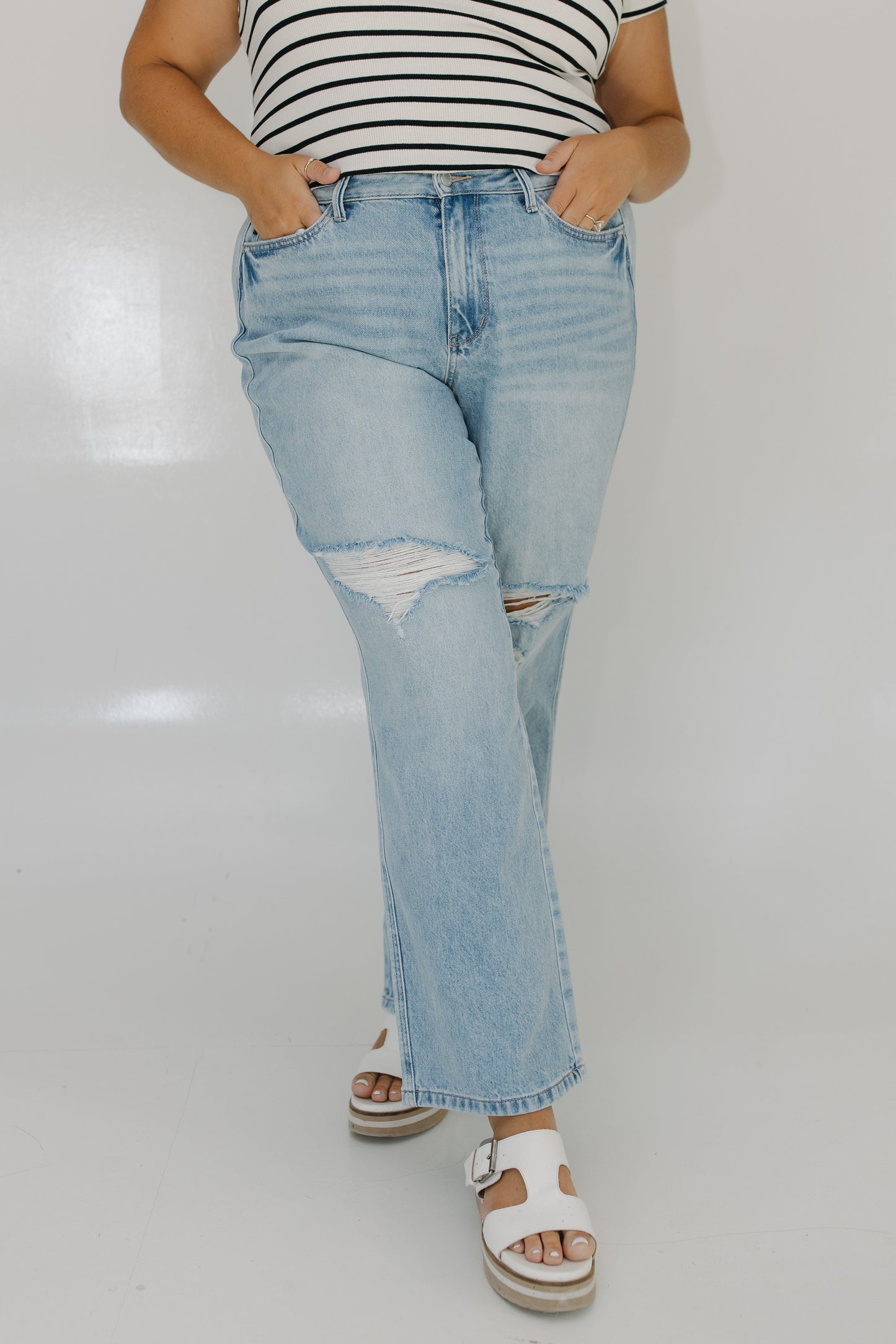 Person wearing light blue ripped jeans and a striped shirt on a white background