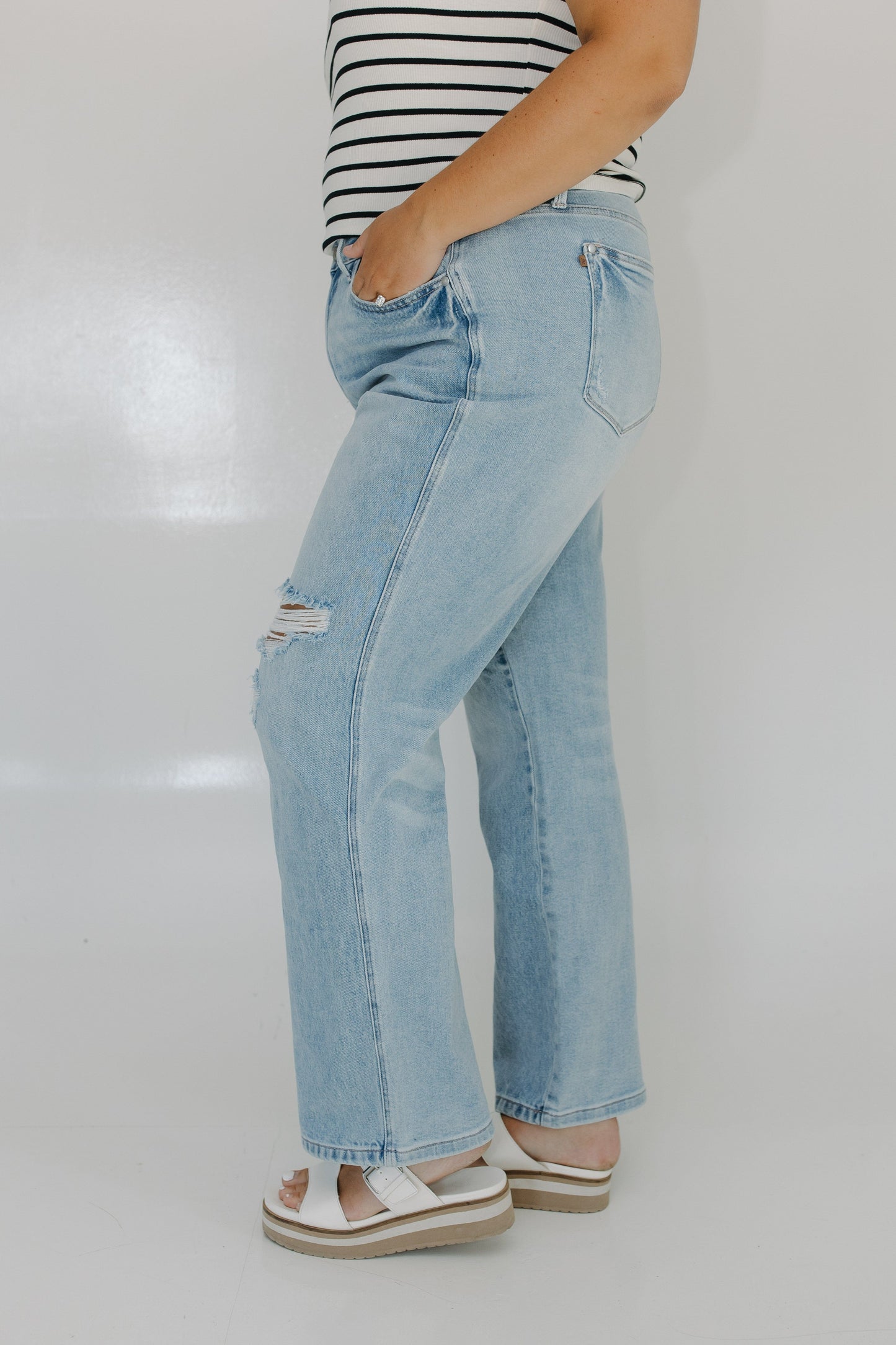 Person wearing light blue jeans and a striped shirt on a plain background