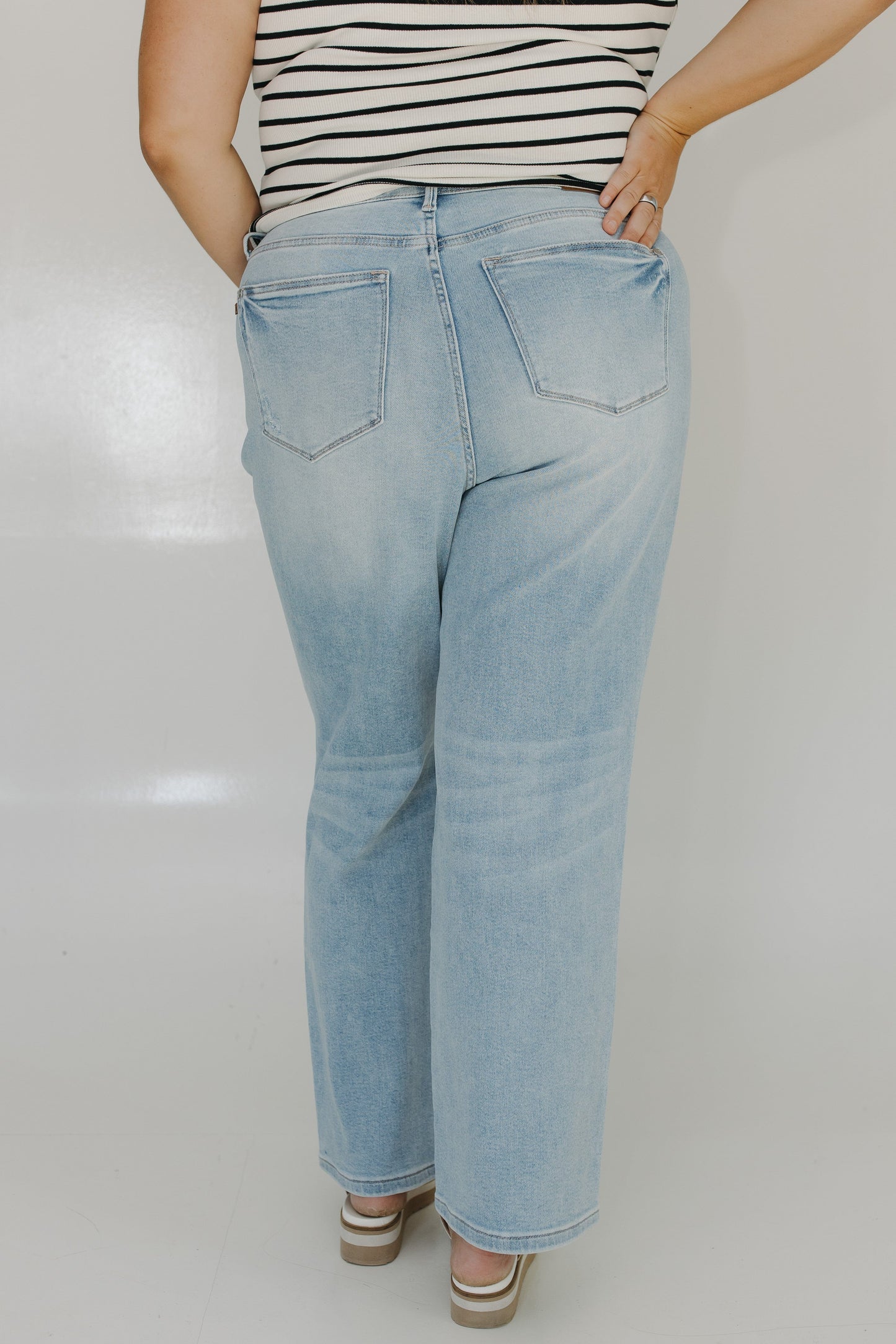 Person wearing light blue jeans and a striped shirt on a plain background
