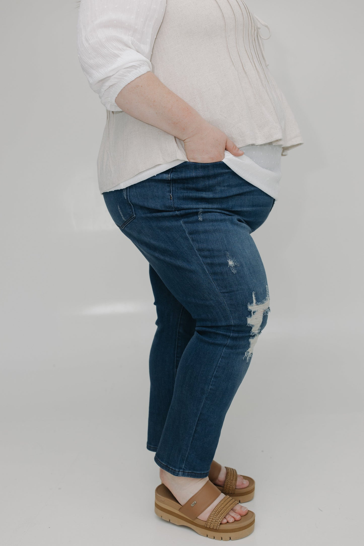 Person wearing blue jeans and a white top on a plain background