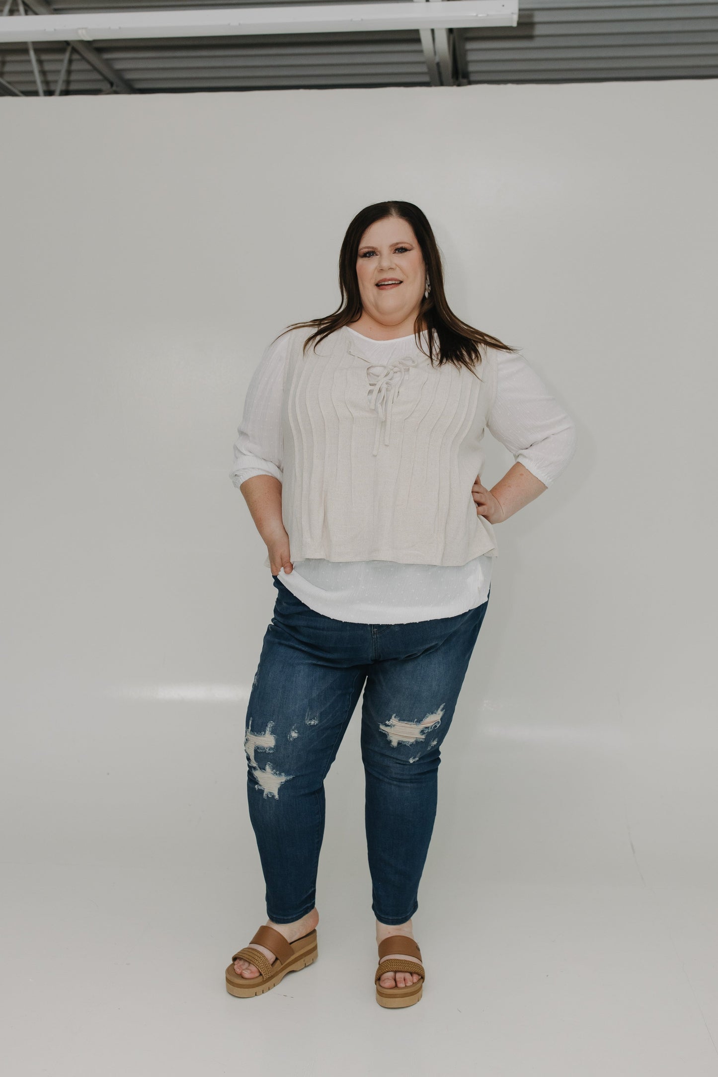 Woman wearing a white sweater and blue jeans standing against a plain background