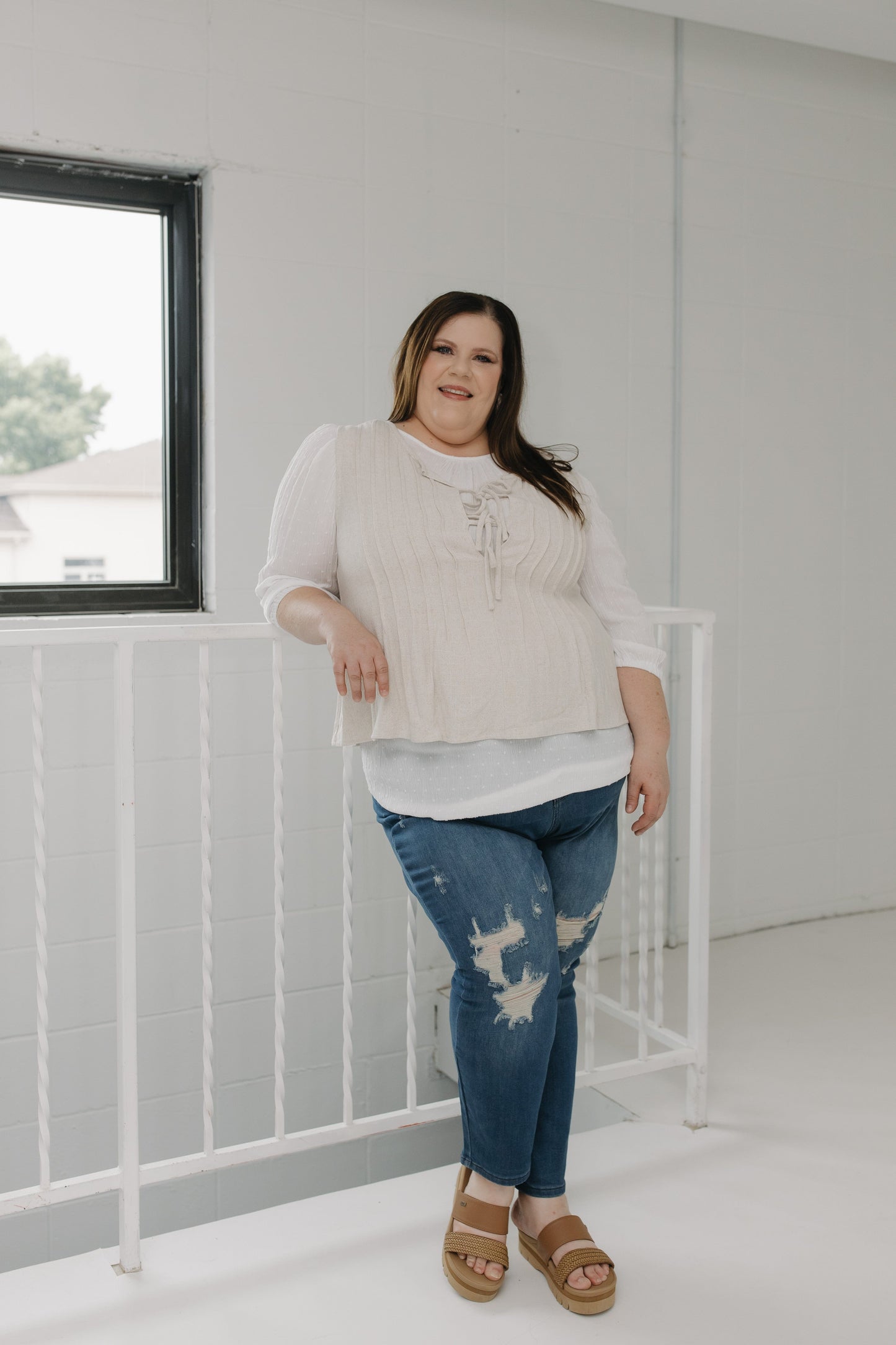 Woman wearing a beige sweater and blue jeans standing in a minimalistic room with a white crib.