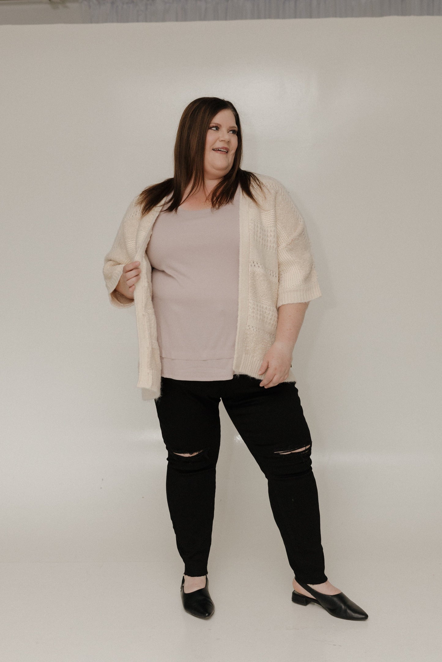 Woman wearing a beige shirt, black pants, and black shoes on a white background