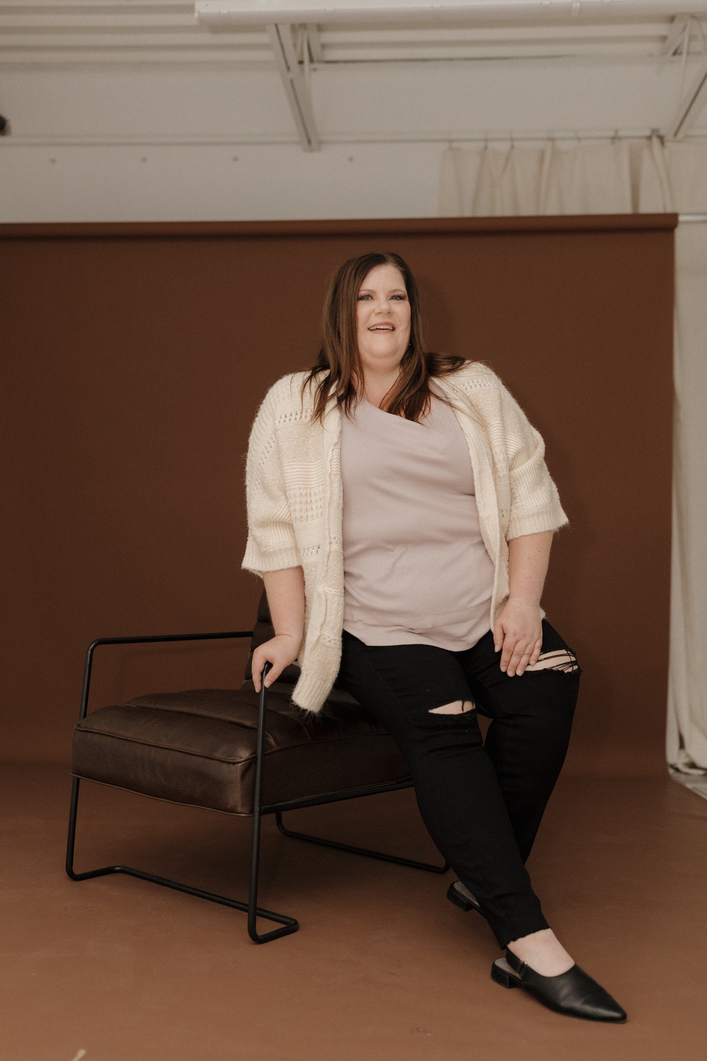 Woman sitting on a chair against a brown wall