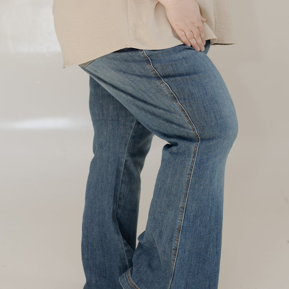 Person wearing blue jeans and a beige top on a plain background