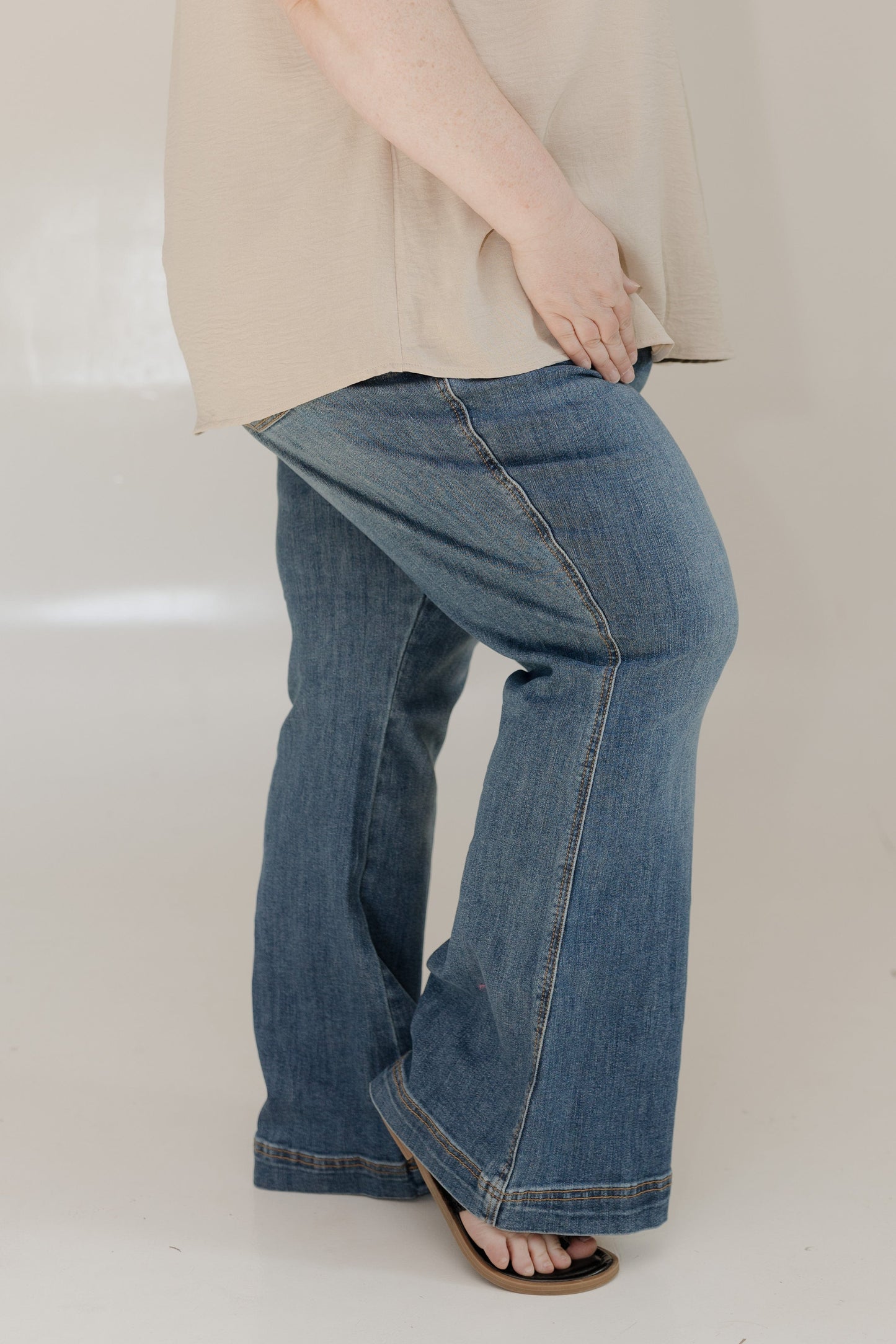 Person wearing blue jeans and a beige top on a plain background