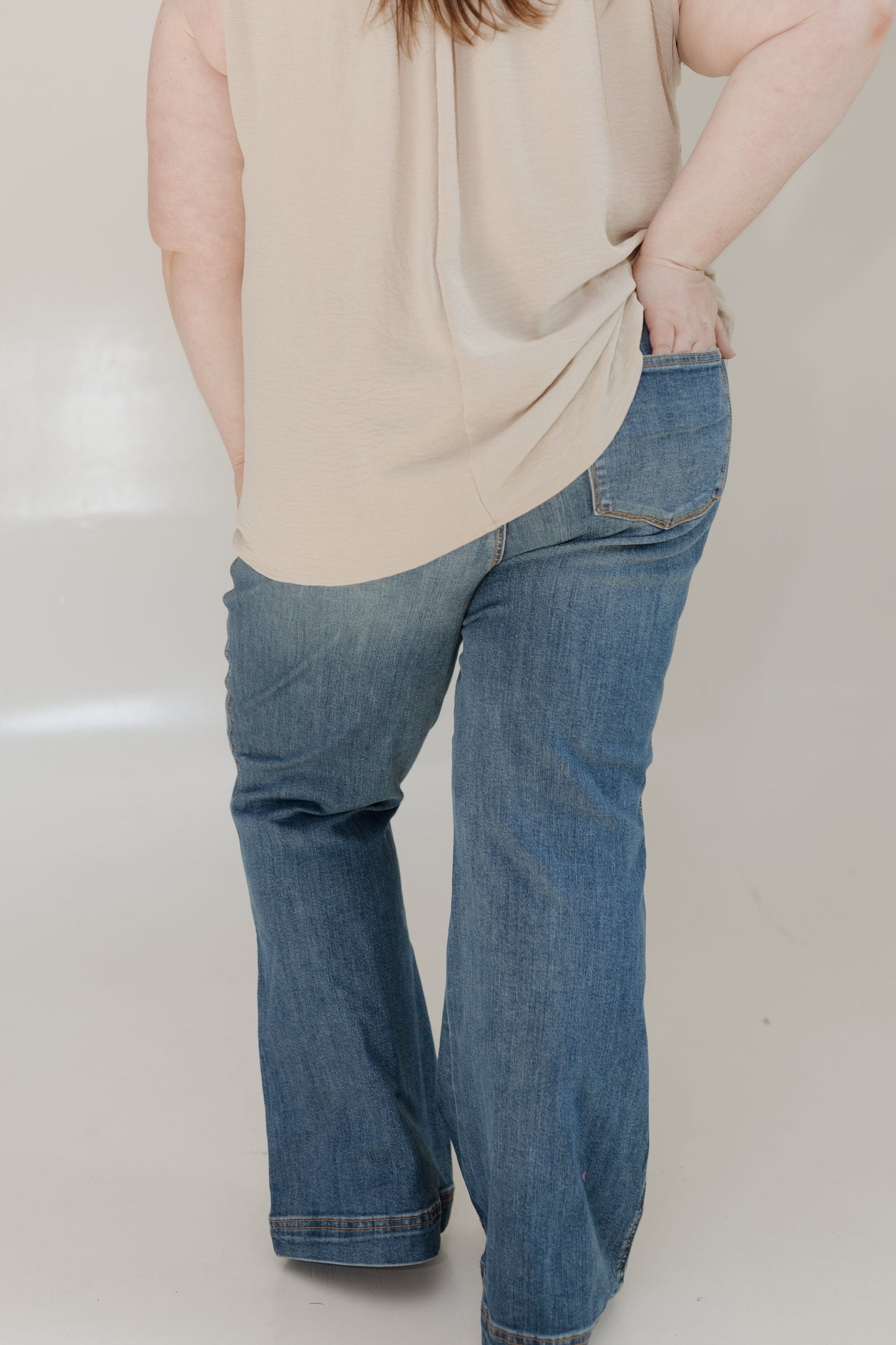 Person wearing a beige sleeveless top and blue jeans on a plain background