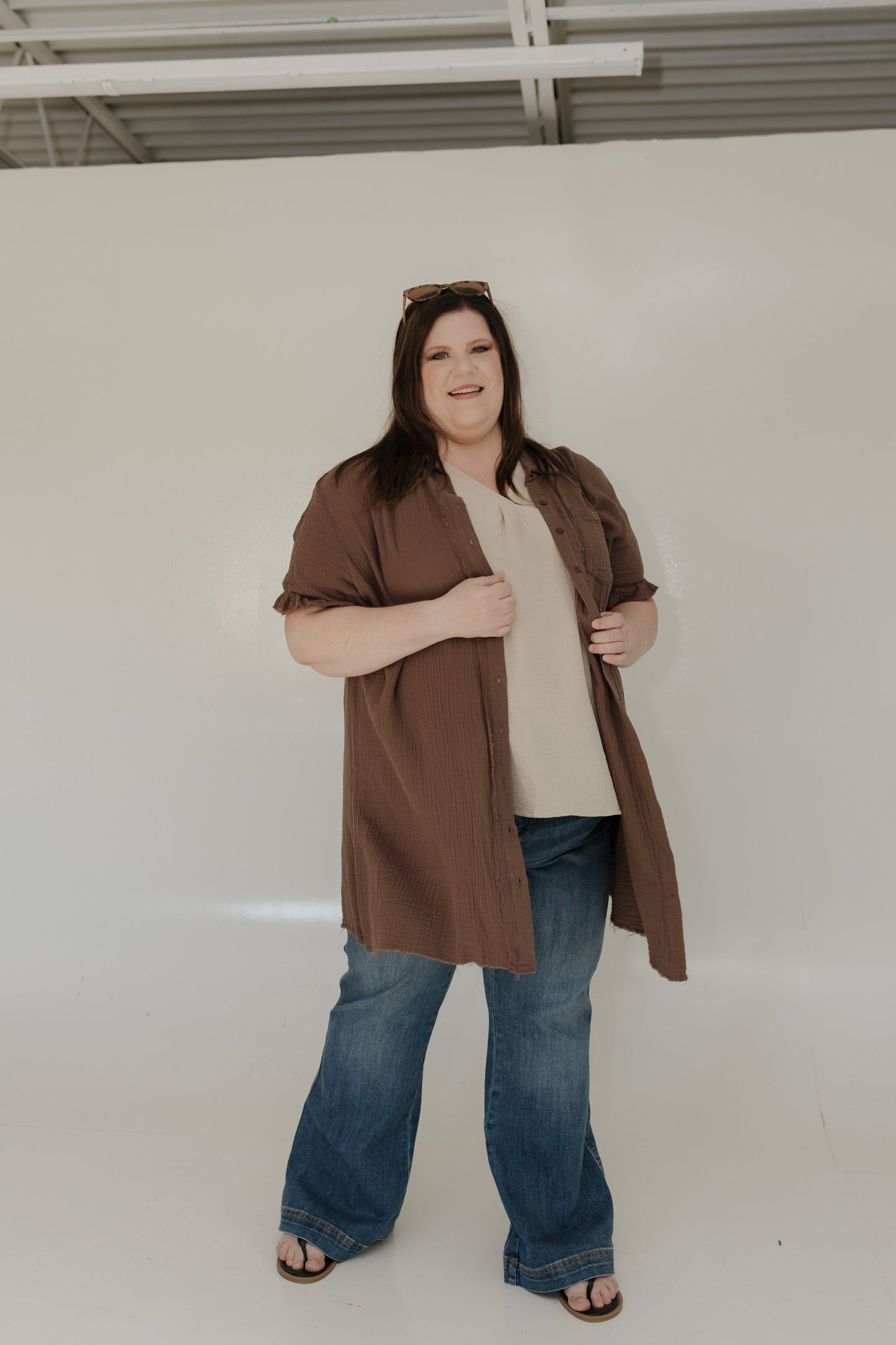 Woman wearing a brown jacket, beige top, and blue jeans against a white background