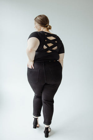 A person with their back facing the camera, wearing black clothing with a crisscross design on the shirt, complemented by JUDY BLUE HIGH WAIST DOUBLE ROLLED CUFFED JOGGER JEANS from Judy Blue and heeled shoes.