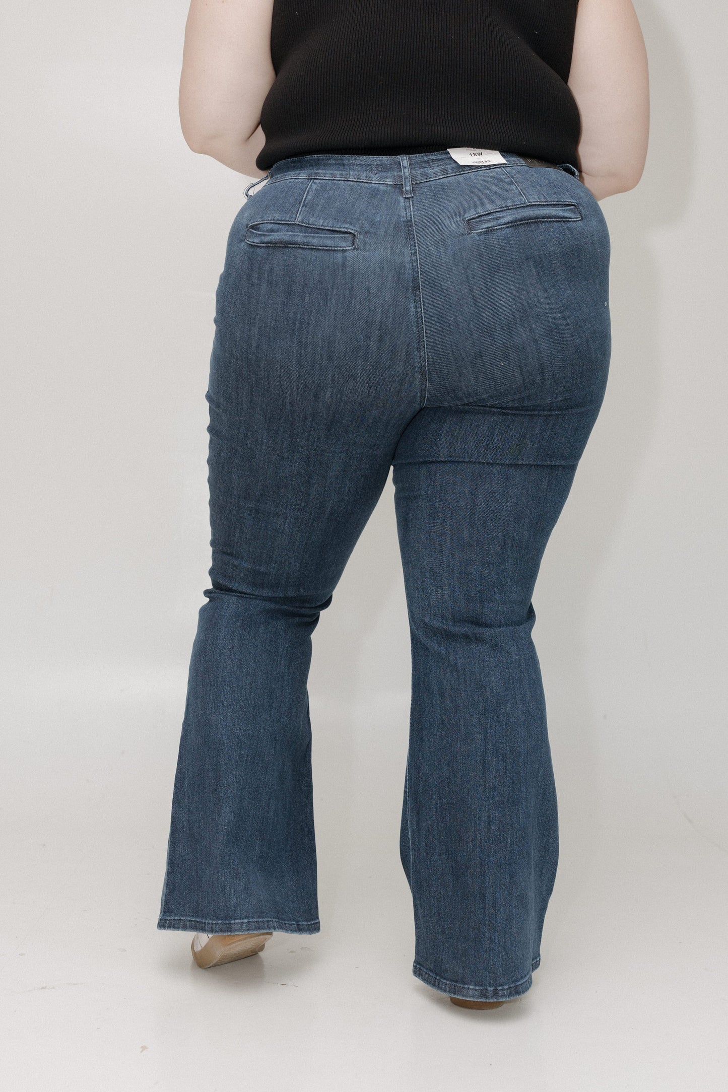 Person wearing blue flared jeans from behind on a plain background