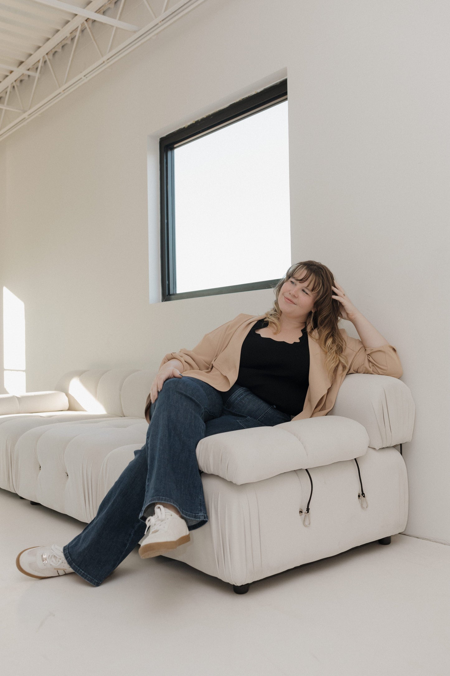 Woman sitting on a white couch in a minimalistic room with large windows.