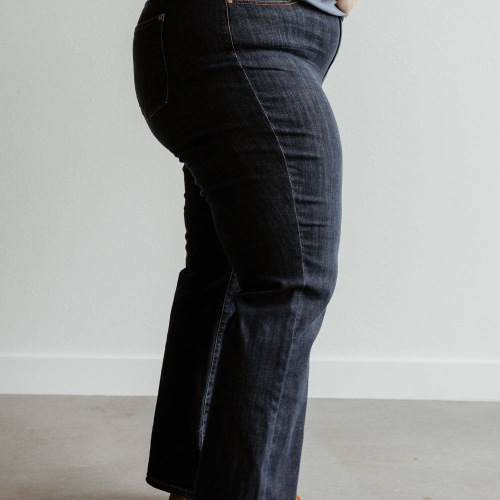 A person wearing a grey top, Judy Blue Jeans, and brown shoes stands side-on against a plain background.