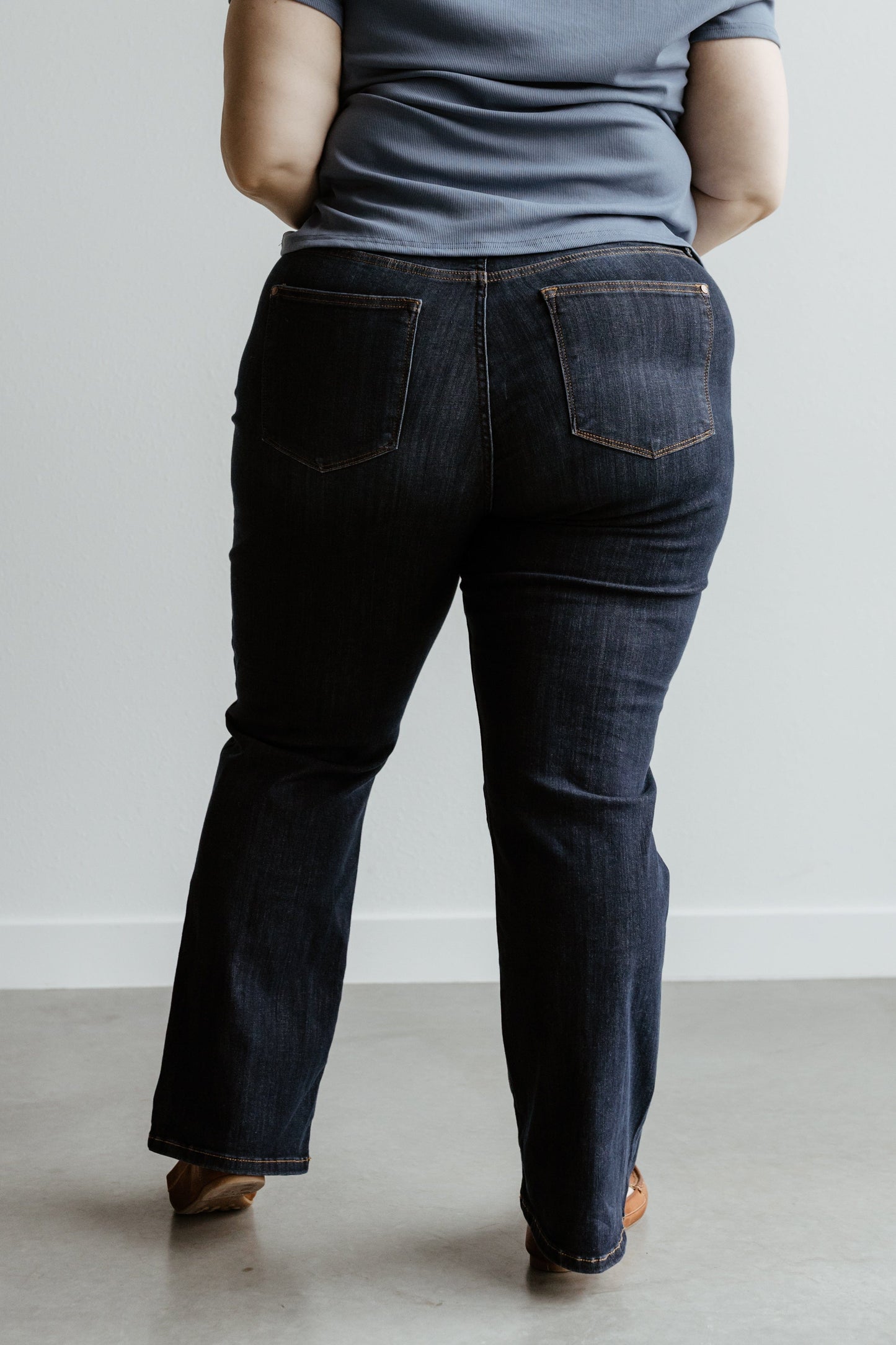 A person in a gray shirt and high waist jeans stands with their back facing the camera.