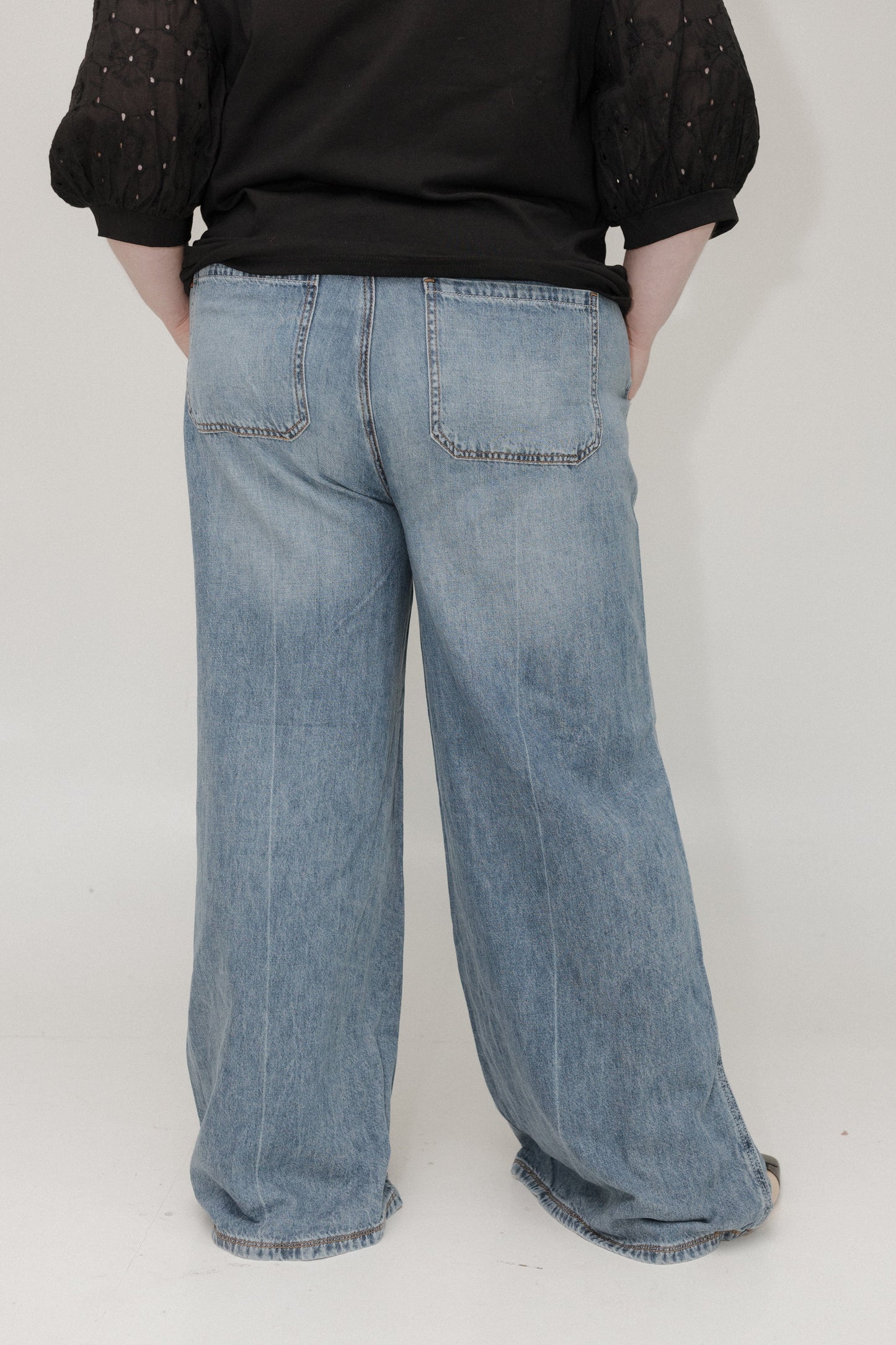 Person wearing light blue jeans and a black top on a white background