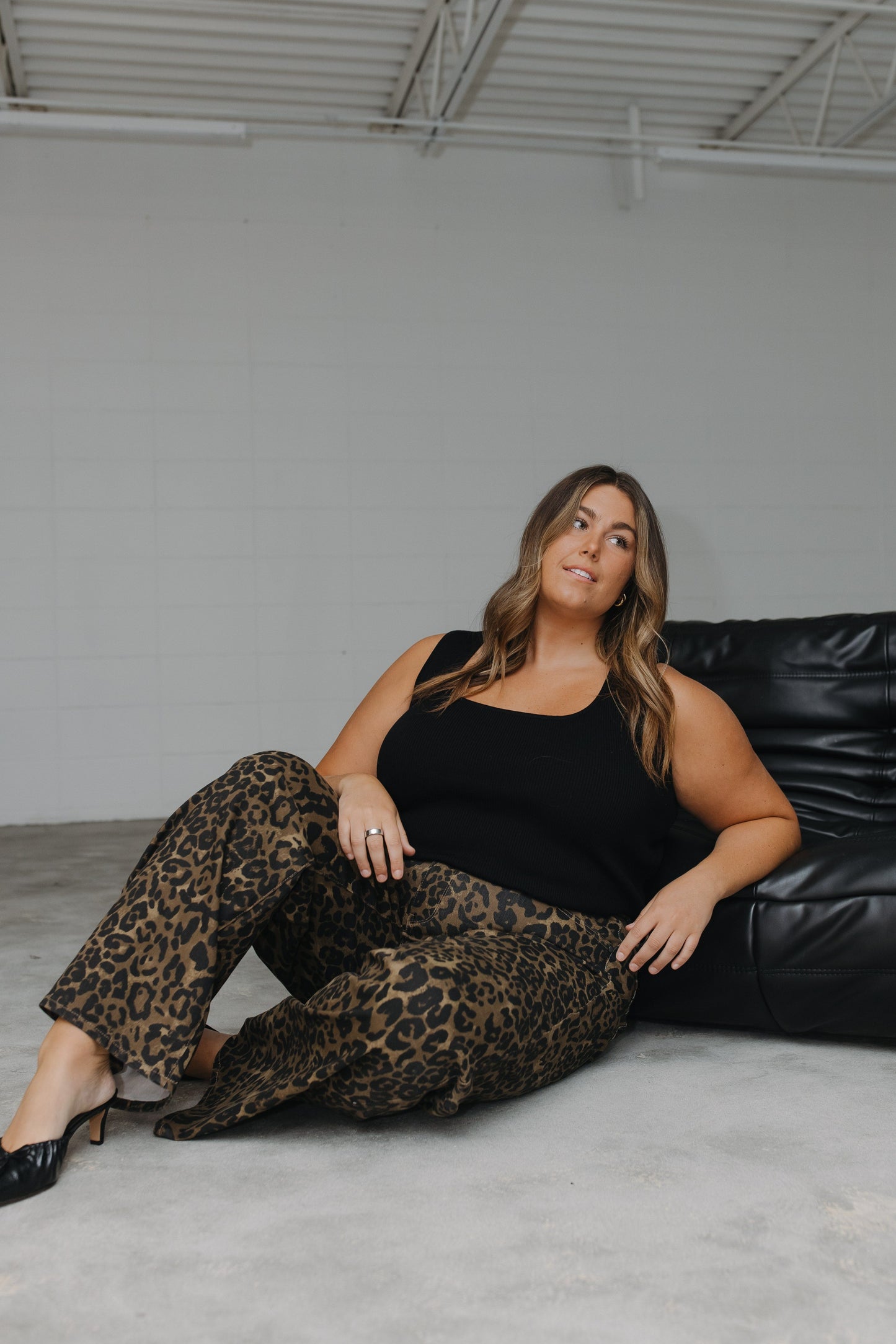 Woman sitting on a black leather couch wearing leopard print pants and a black top.