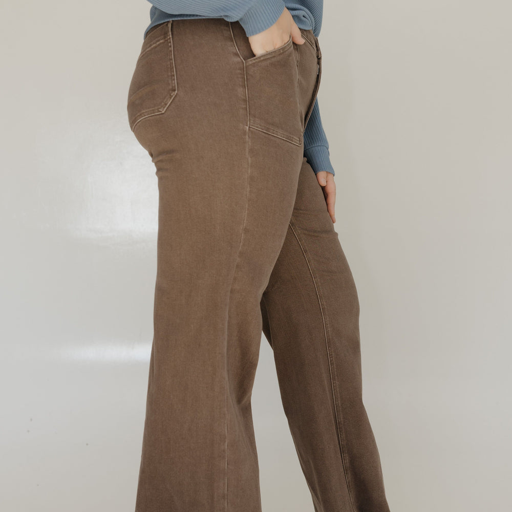 Person wearing brown wide-leg pants and a blue sweater on a plain background