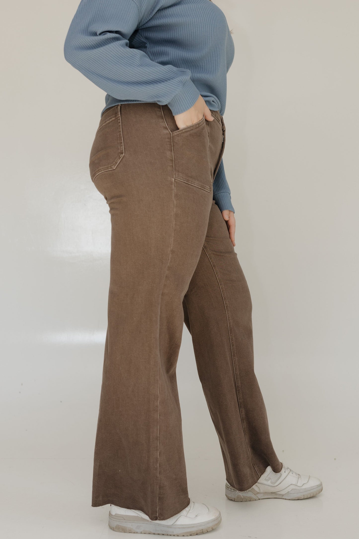 Person wearing brown wide-leg pants and a blue sweater on a plain background