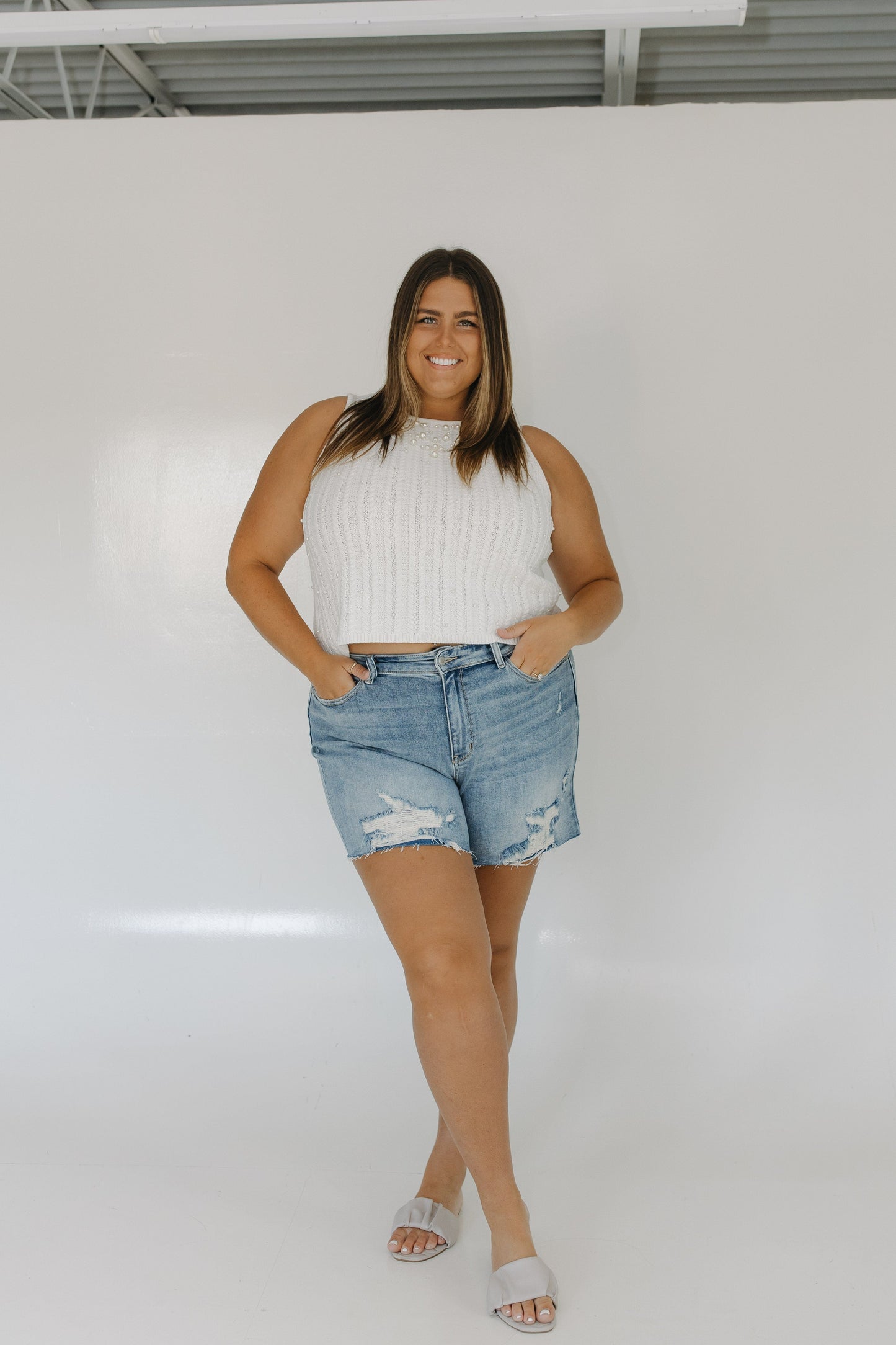 Woman wearing a white ribbed top and denim shorts against a white background
