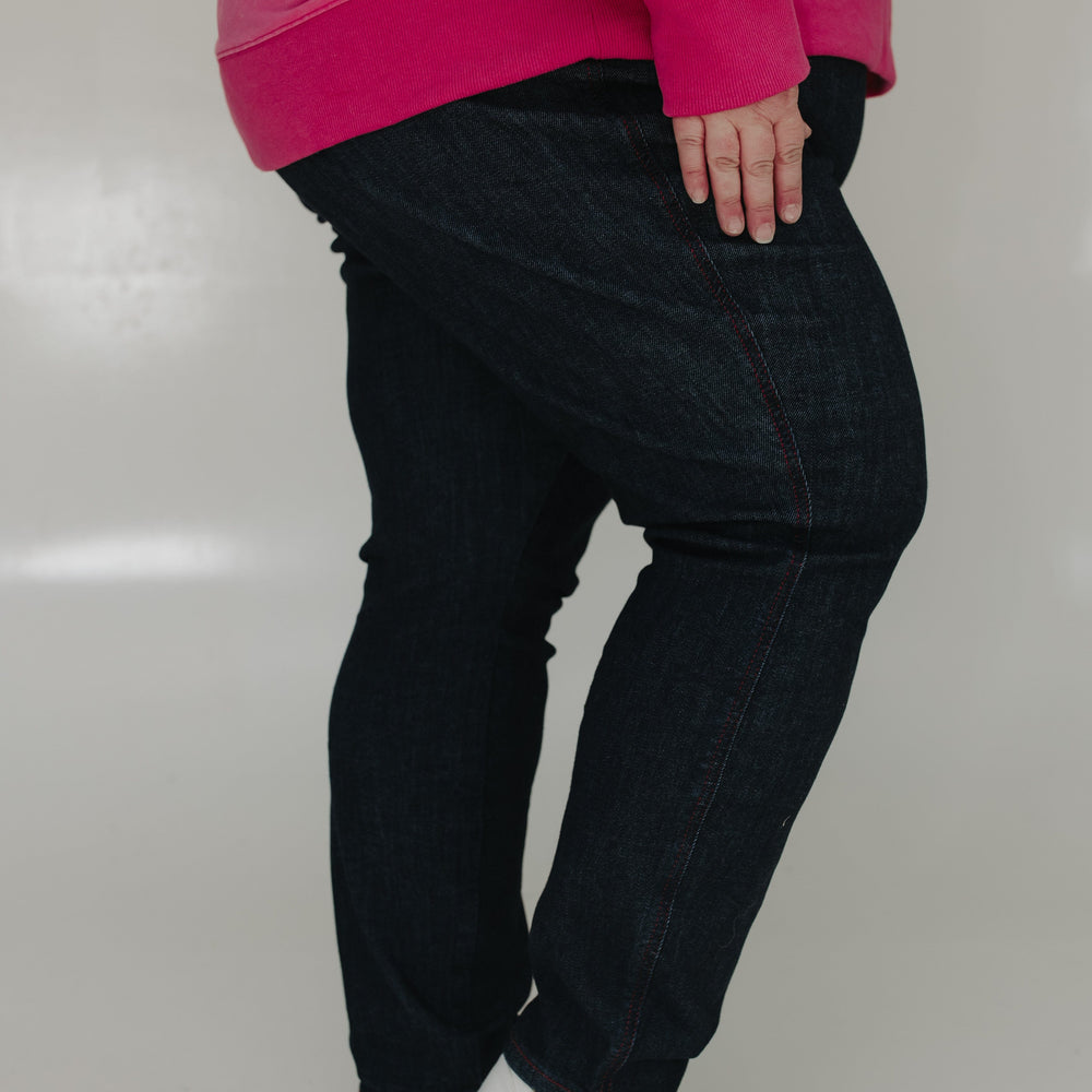 Person wearing a bright pink sweatshirt, black pants, and white shoes on a plain background