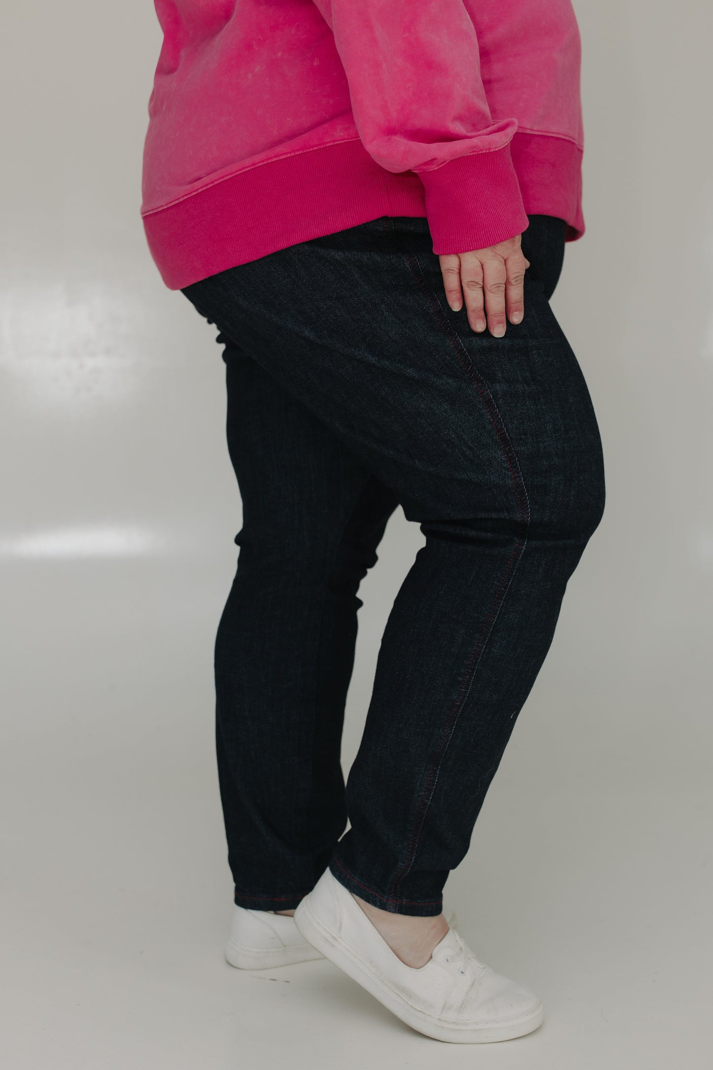 Person wearing a bright pink sweatshirt, black pants, and white shoes on a plain background