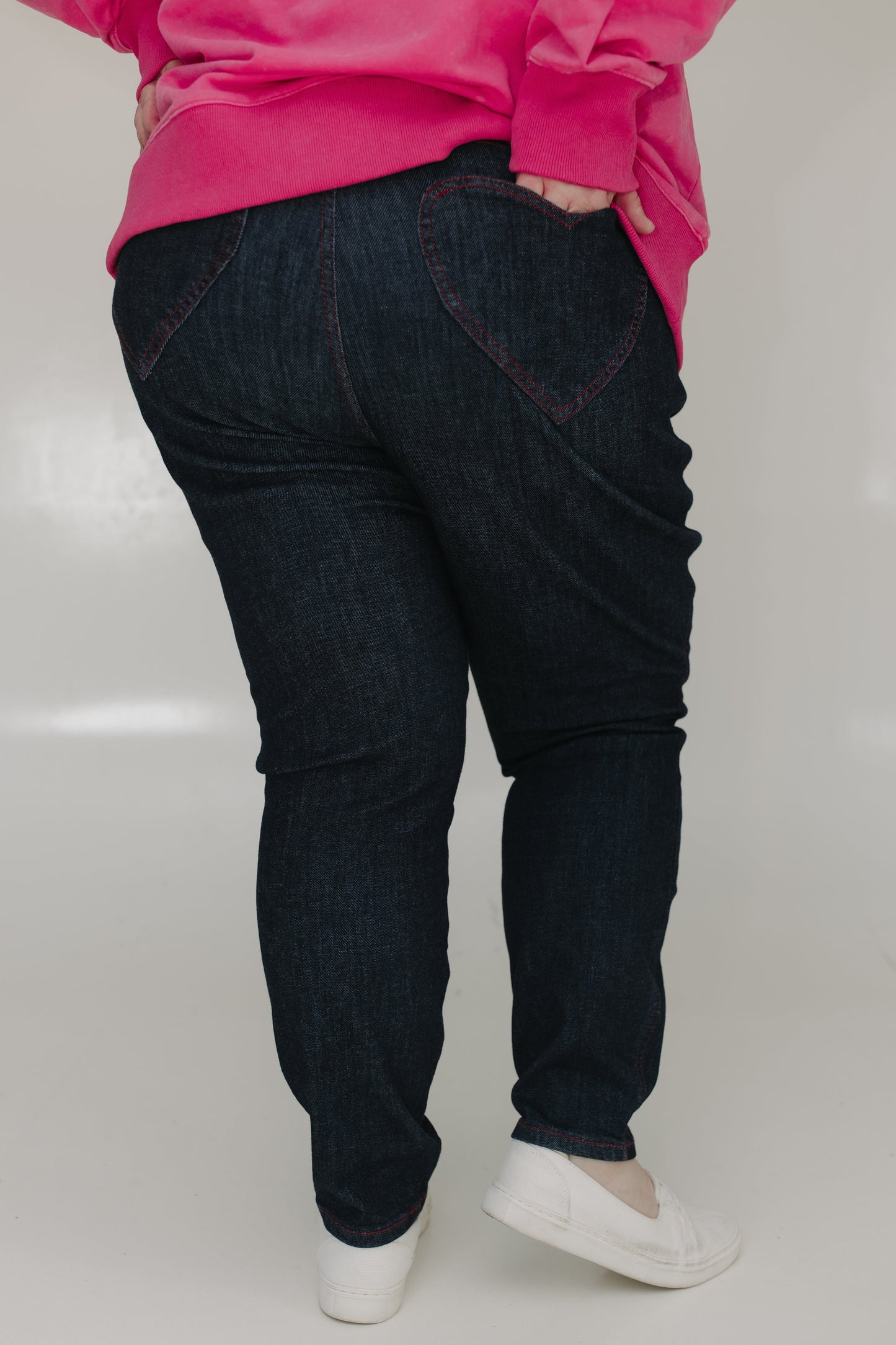 Person wearing dark blue jeans and a pink top on a white background