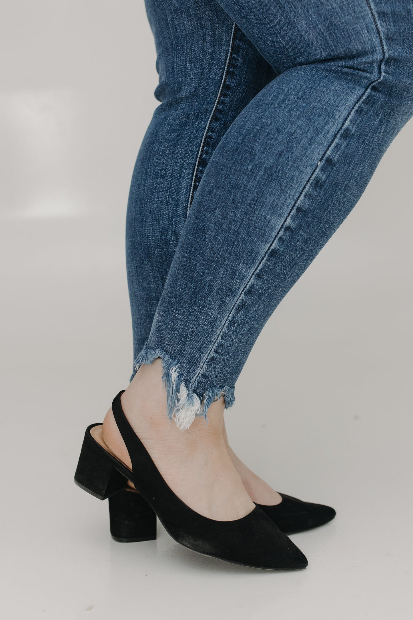 Person wearing blue jeans and black high-heeled shoes on a light gray background