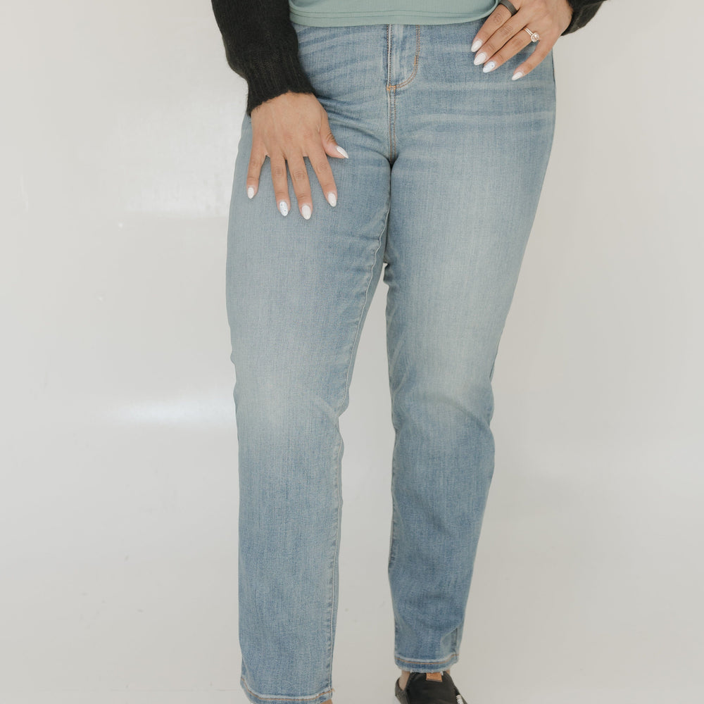 Person wearing light blue jeans and black shoes on a plain background
