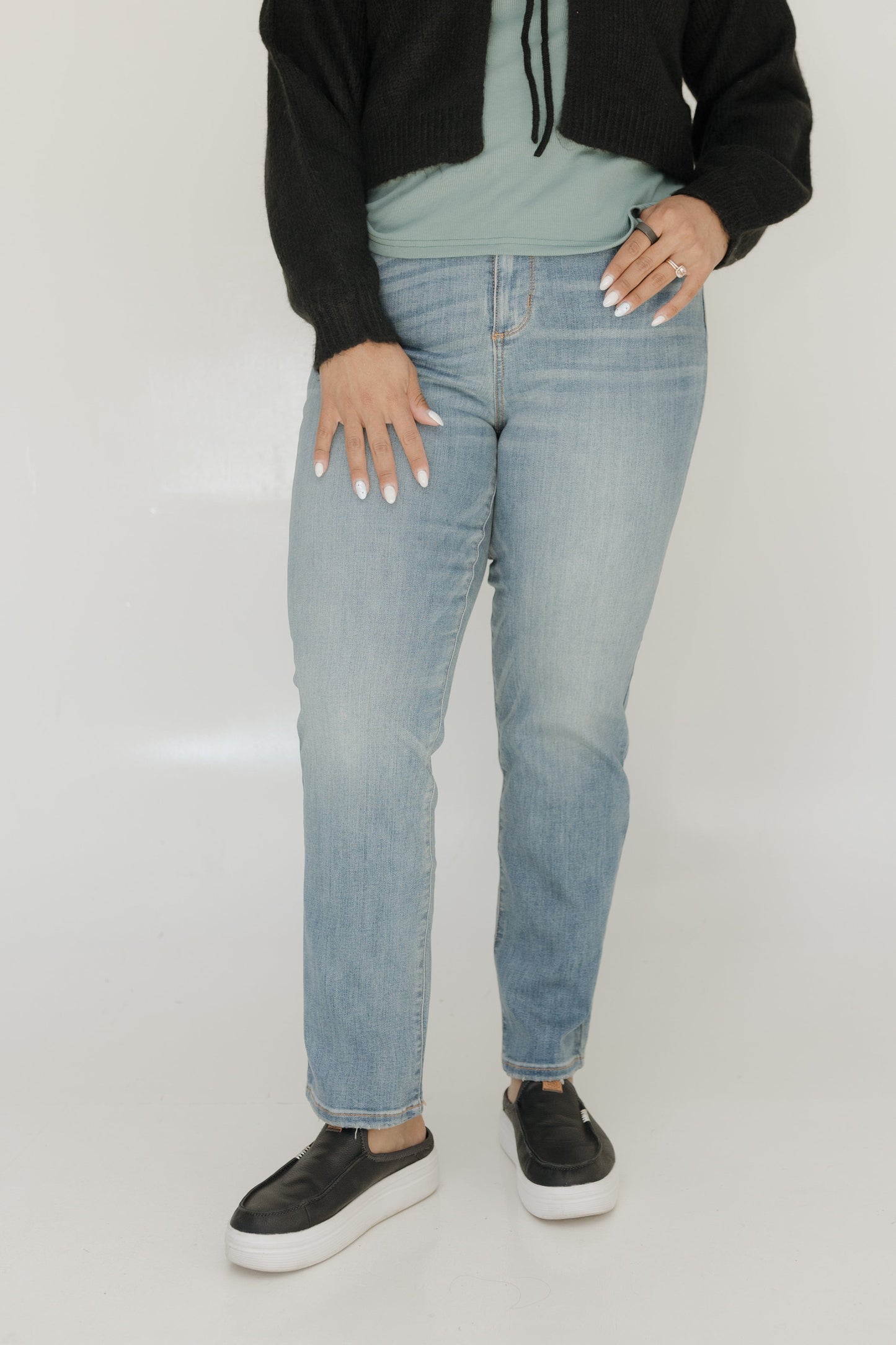 Person wearing light blue jeans and black shoes on a plain background