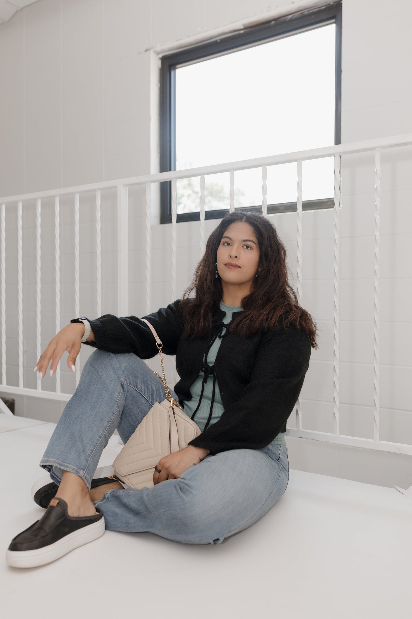 Person sitting on a bed in a minimalistic room with white walls and a large window.