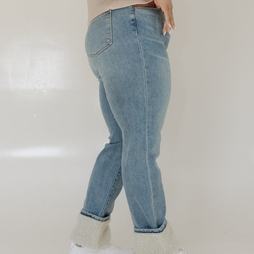 Person wearing light blue jeans and white sneakers on a plain background